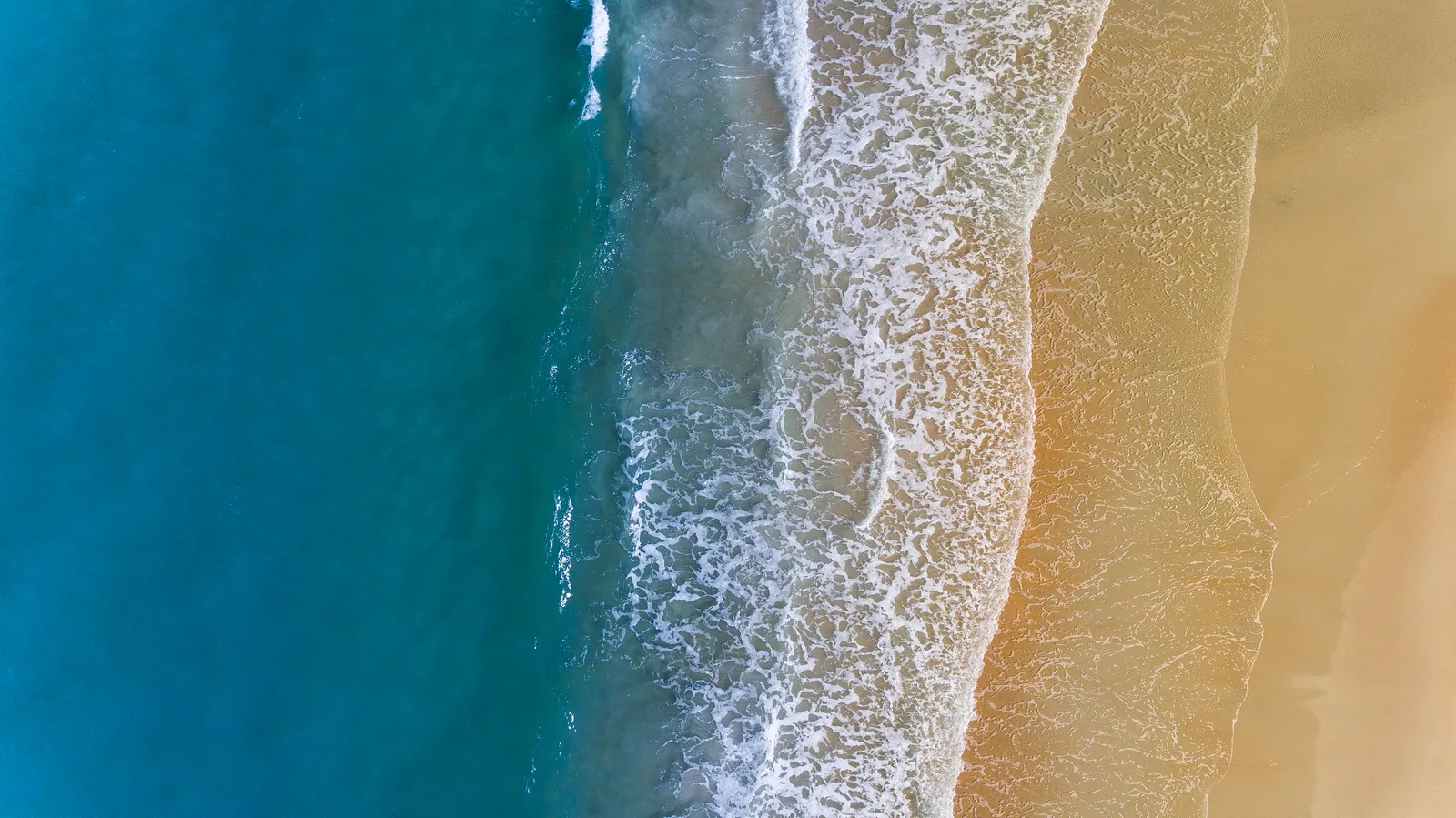 Turquoise ocean waves rolling onto a sandy beach, seen from above
