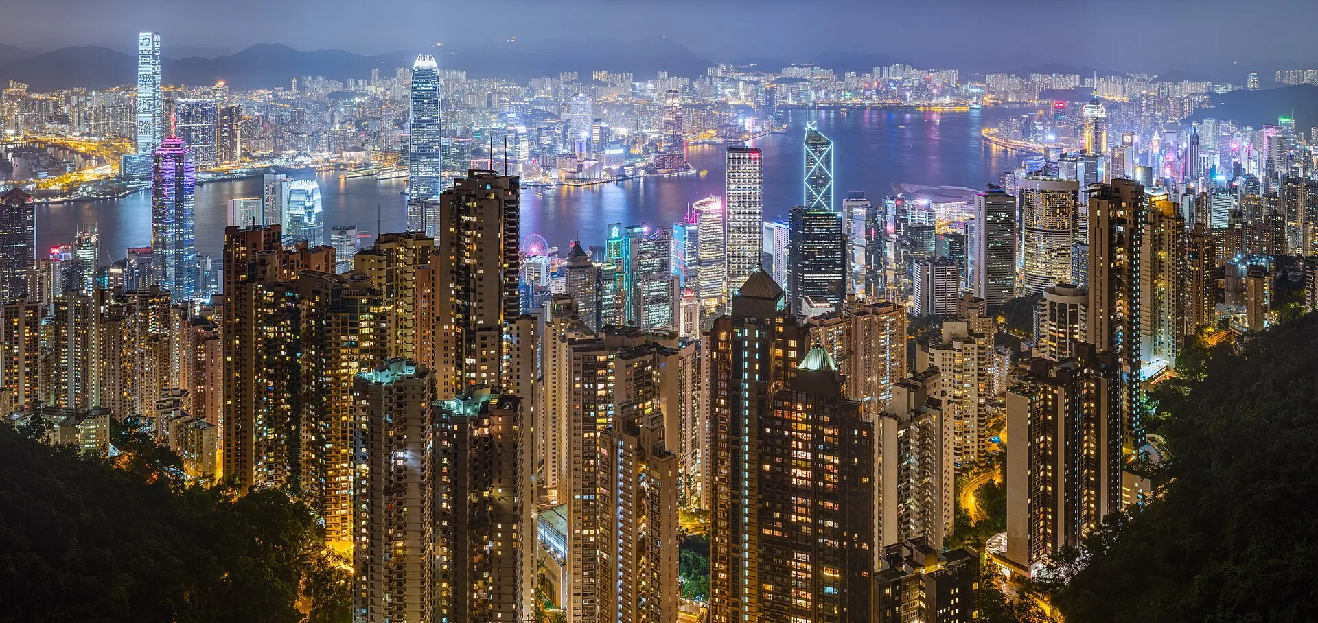 A dense city skyline lit up at night over the harbor