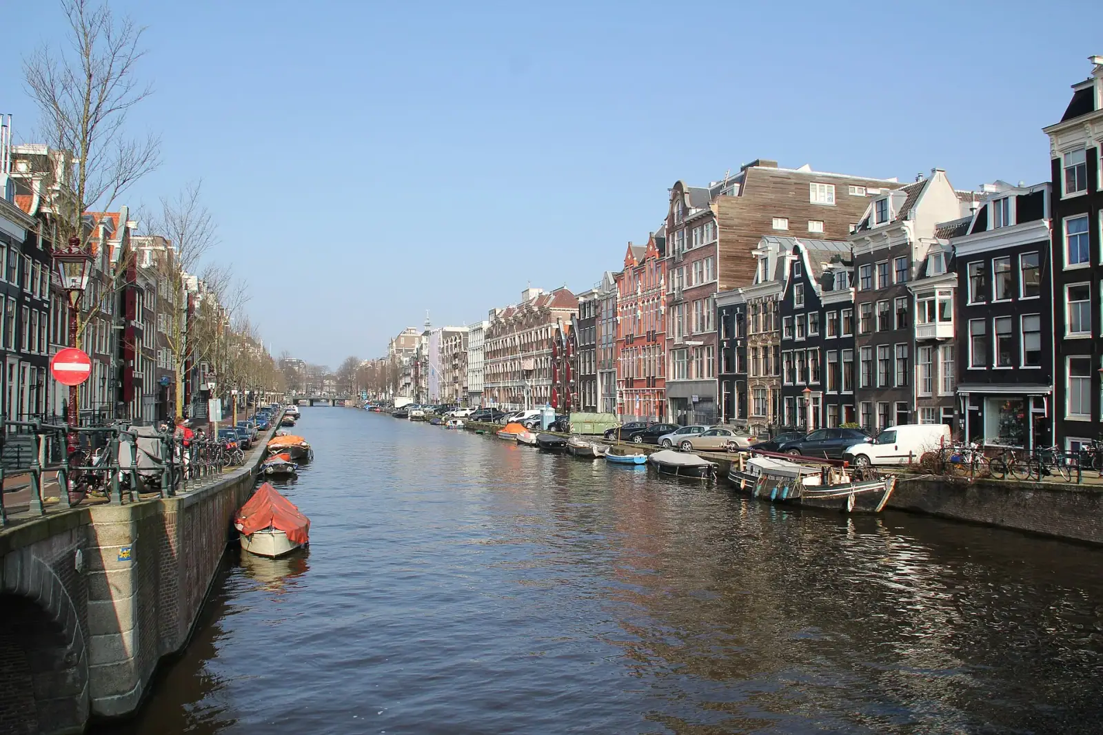 Amsterdam canal lined with gabled Dutch canal houses and moored boats under a clear blue sky