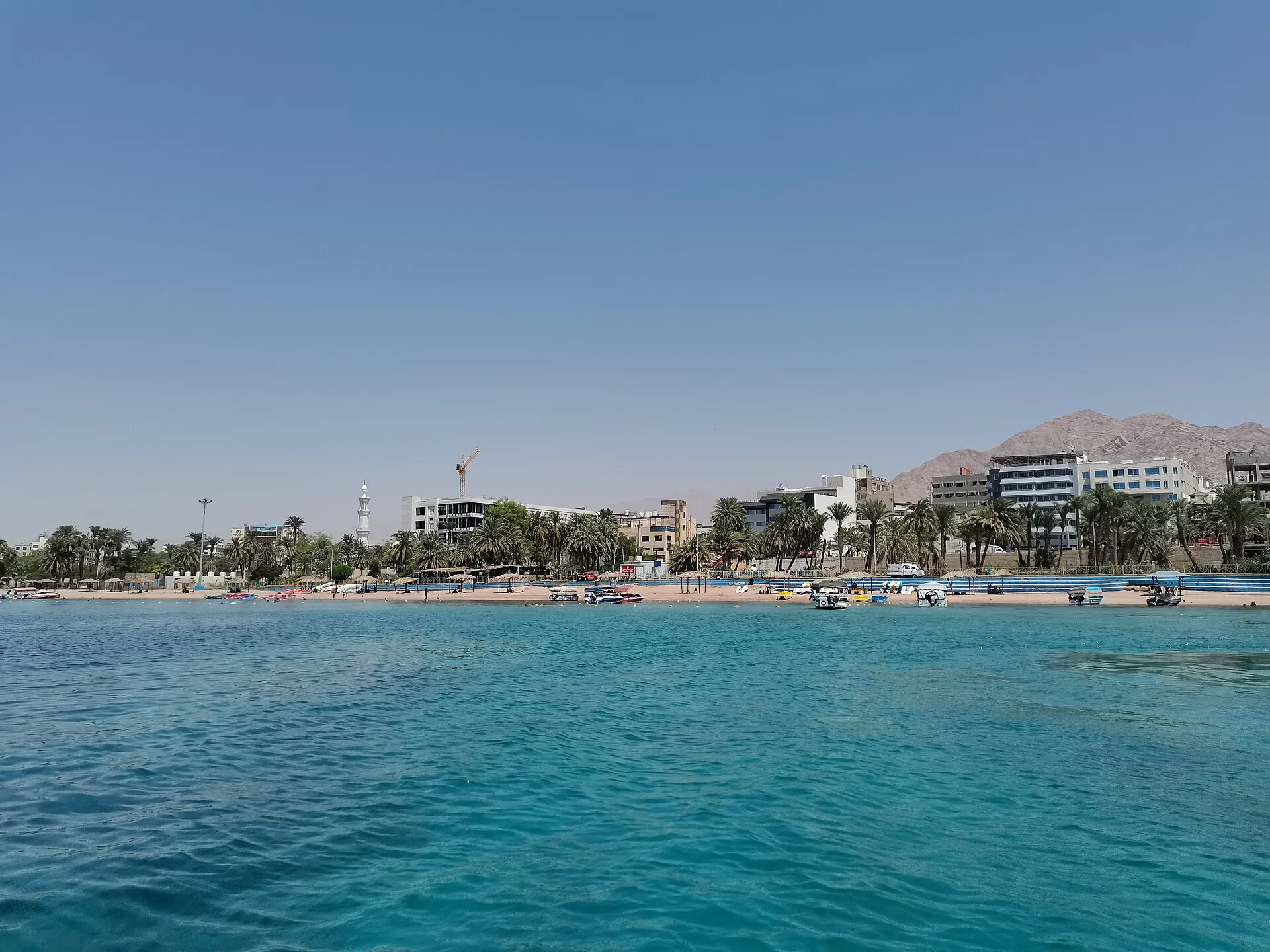 Aqaba waterfront with turquoise Red Sea, city skyline, mosque minaret, palm trees and rocky mountains