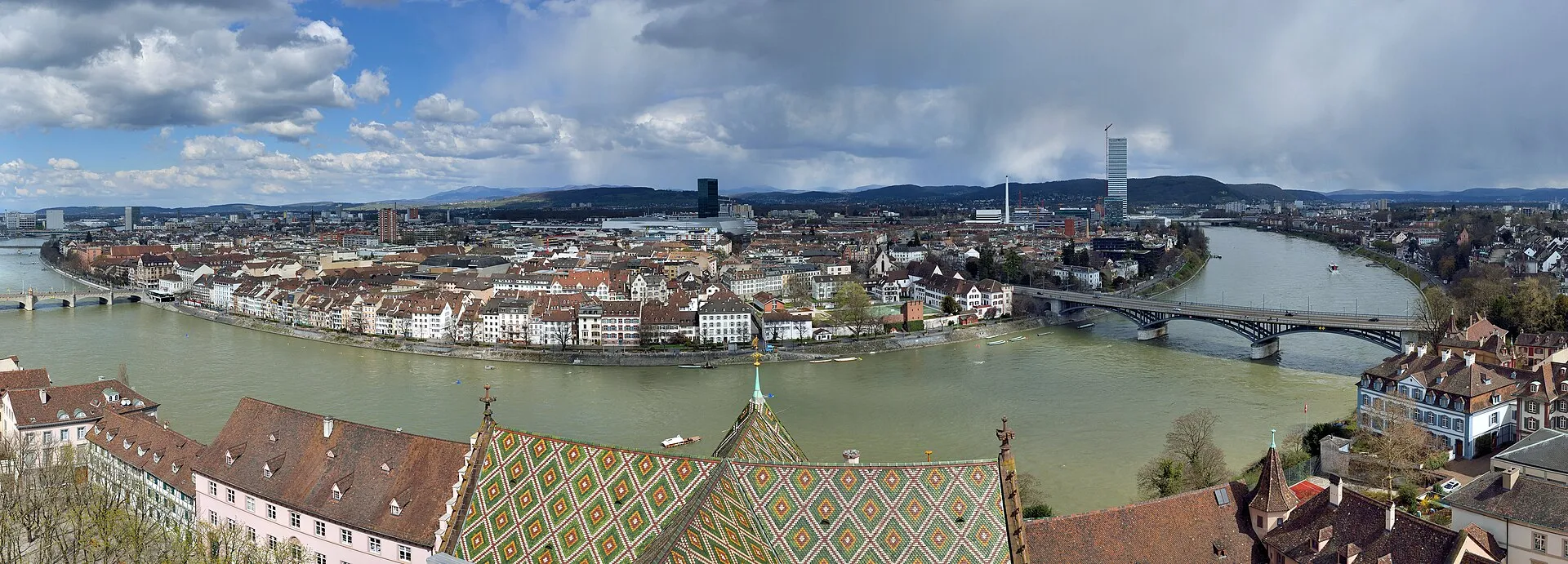 Panoramic view of Basel from the Minster tower, showing the Rhine bend, city skyline, and Minster's colorful tiled roof