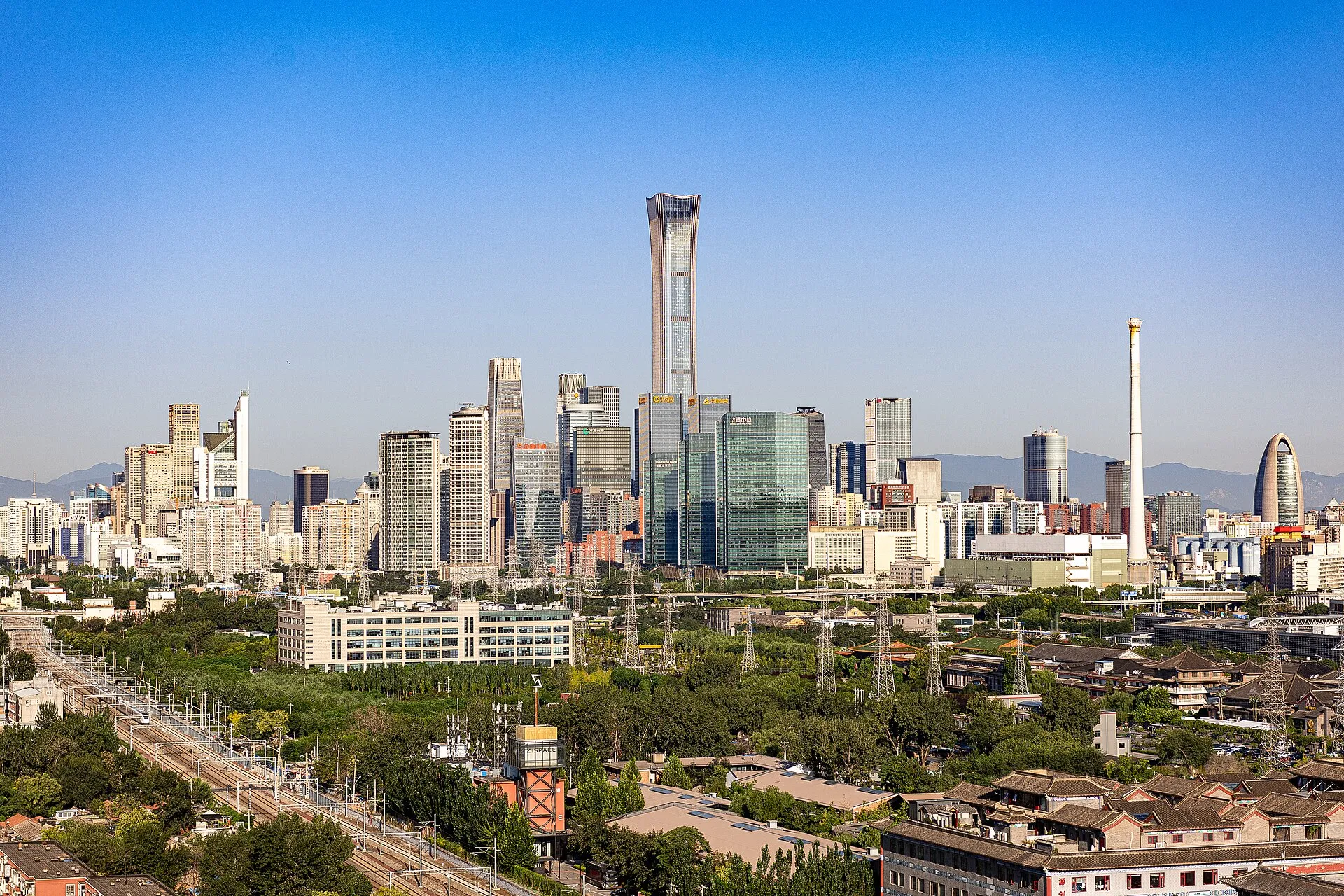 The Beijing CBD skyline in clear daylight with the tapered CITIC Tower rising above Guomao and distant mountains on the horizon