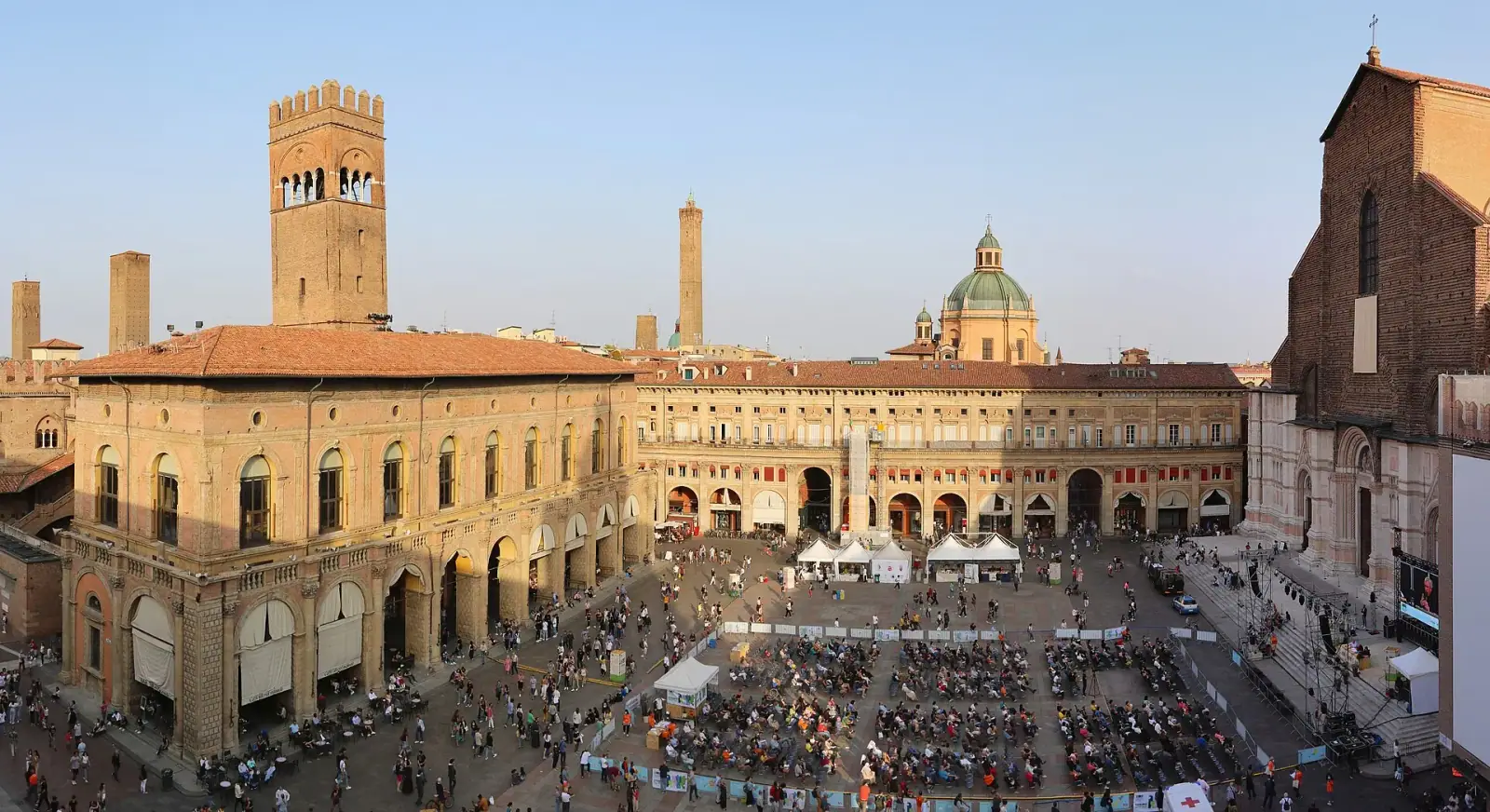 Piazza Maggiore in Bologna seen from above at golden hour, showing Palazzo del Podesta, Torre degli Asinelli, and San Petronio Basilica