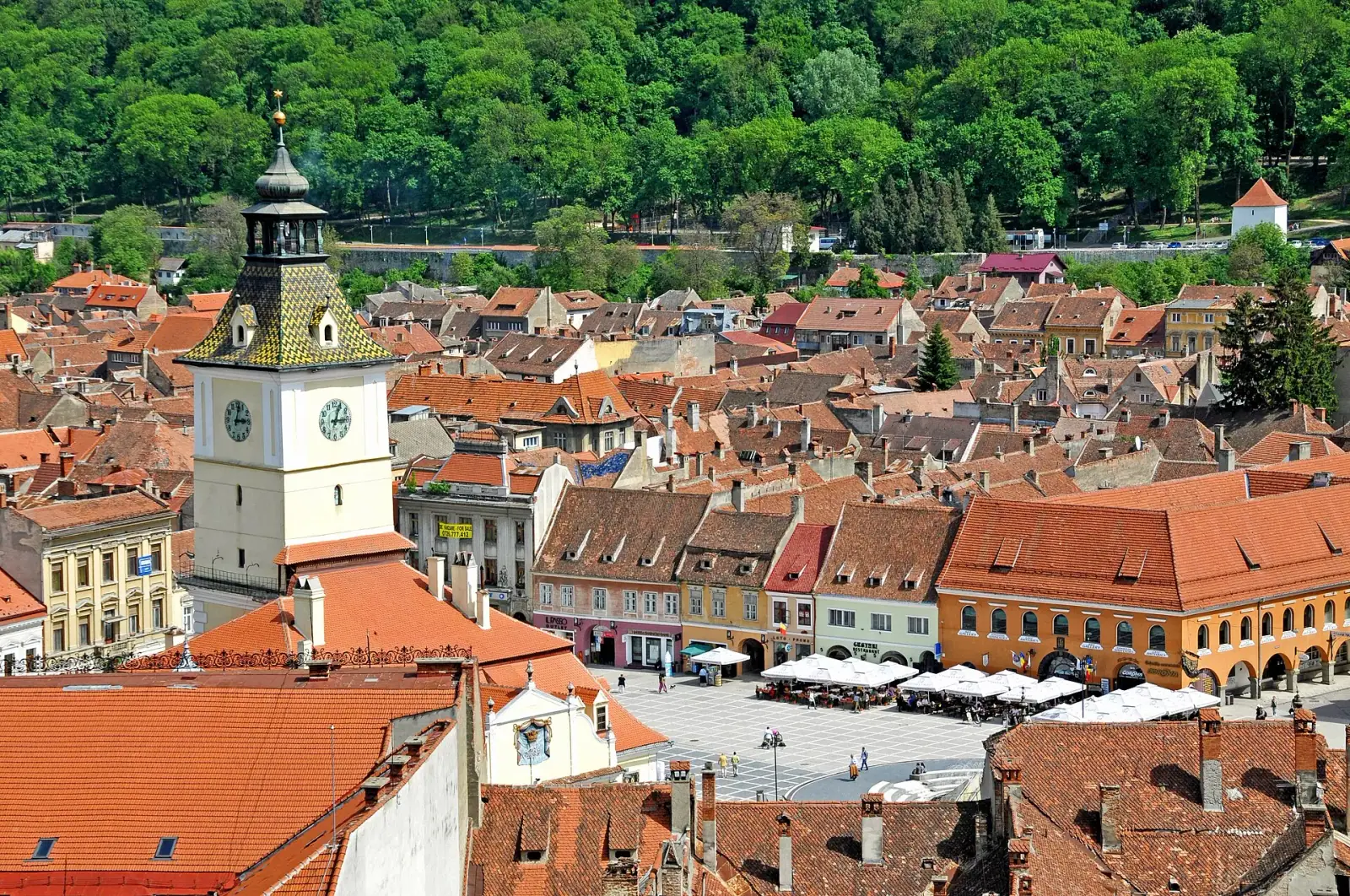 Aerial view of Brașov old town with Council Square and Council House tower surrounded by red-roofed buildings and forested hills