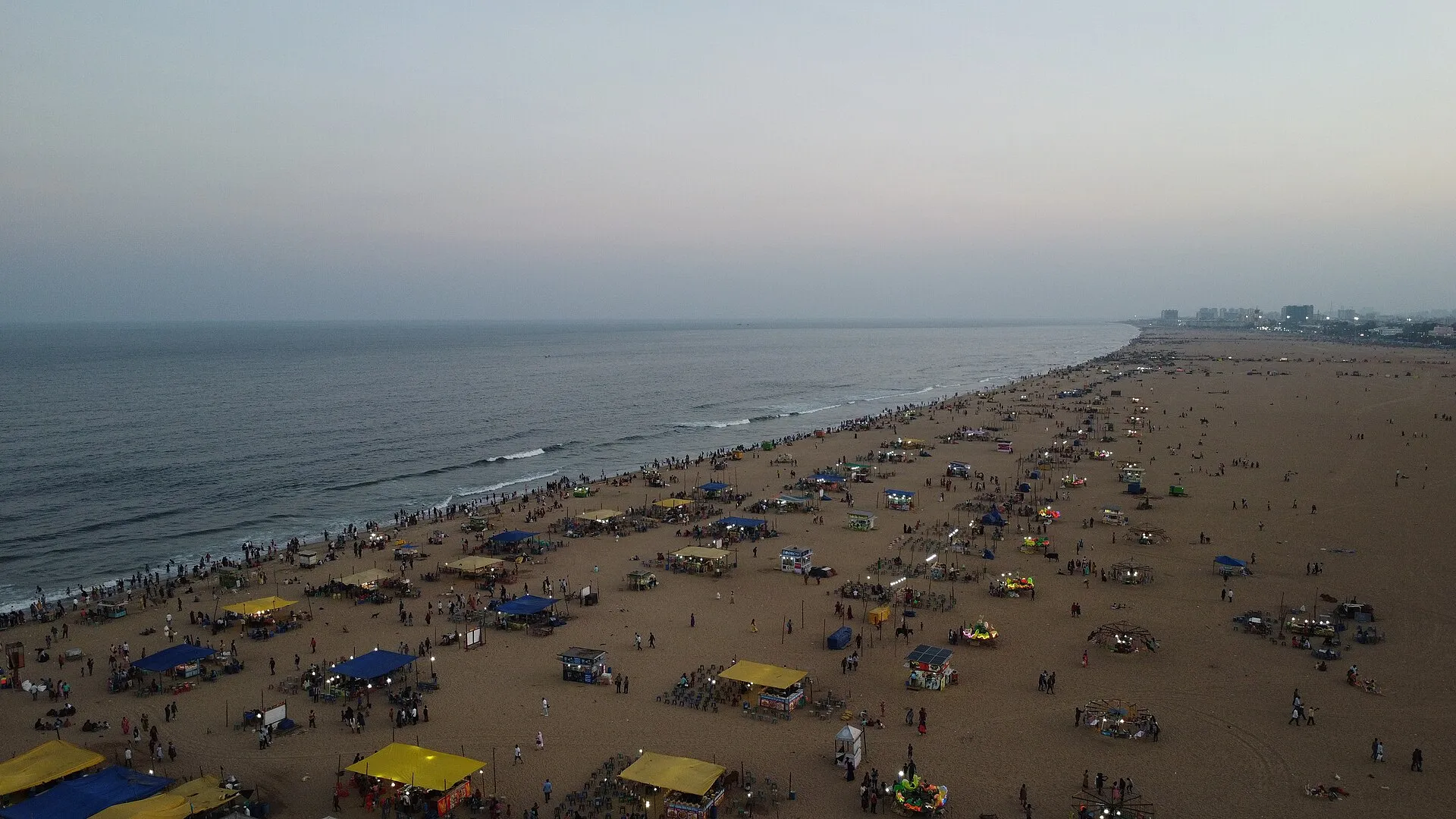 Aerial view of crowds and food stalls along Marina Beach in Chennai at dusk