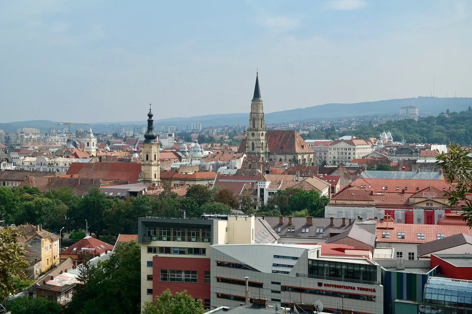 Cluj-Napoca cityscape viewed from Cetătuia Park, showing St. Michael's Church and red-tiled rooftops