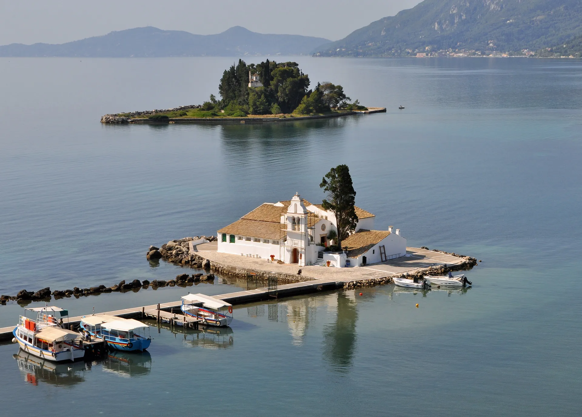 The white Vlacherna Monastery on its tiny islet linked by a causeway at Kanoni, Corfu, with the cypress-topped Mouse Island (Pontikonisi) behind on the calm blue Ionian Sea
