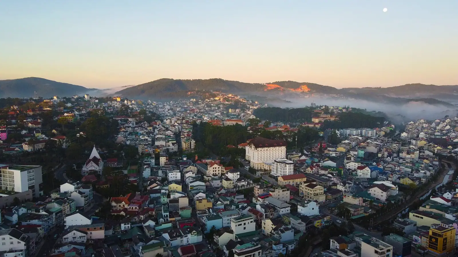 Aerial view of Da Lat cityscape at dawn with misty mountains and colourful rooftops, Vietnam