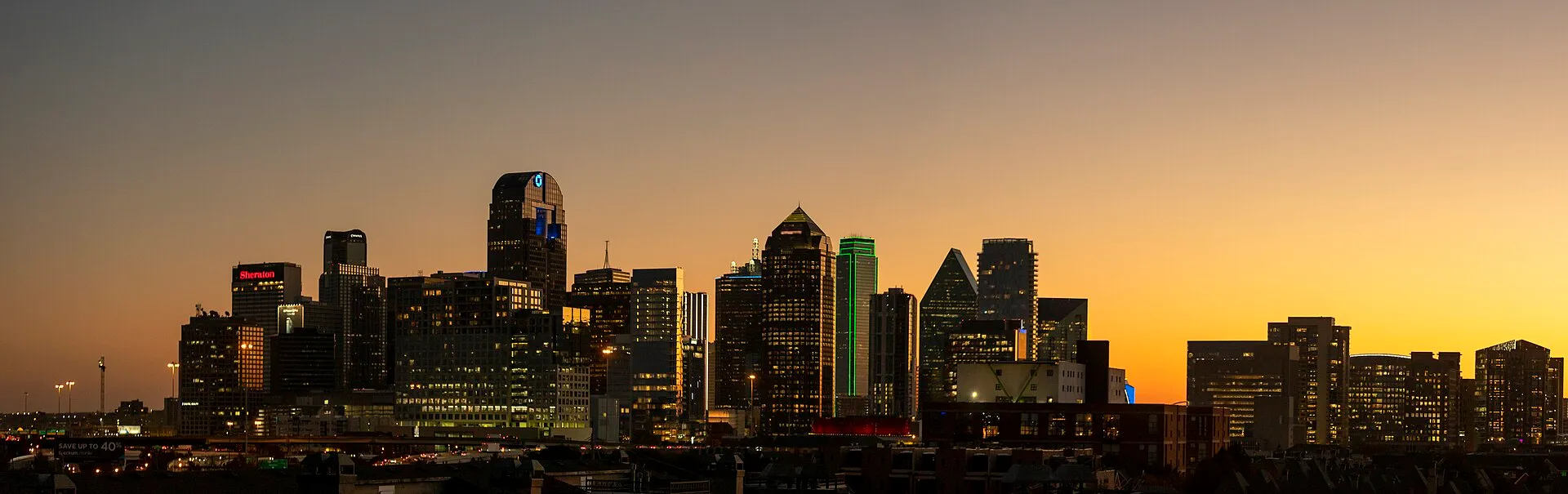 The Dallas downtown skyline silhouetted against a warm orange and gold dusk sky
