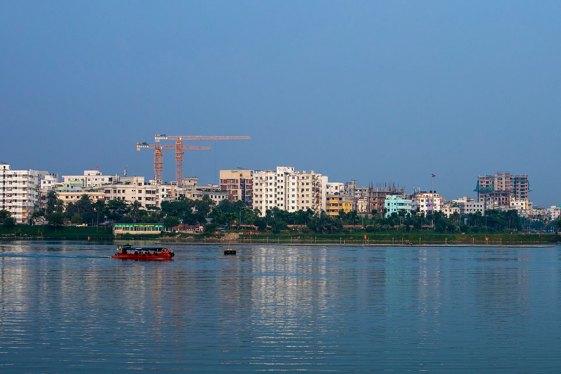 Apartment blocks and a small passenger boat along the calm water of Hatirjheel Lake in central Dhaka, Bangladesh.