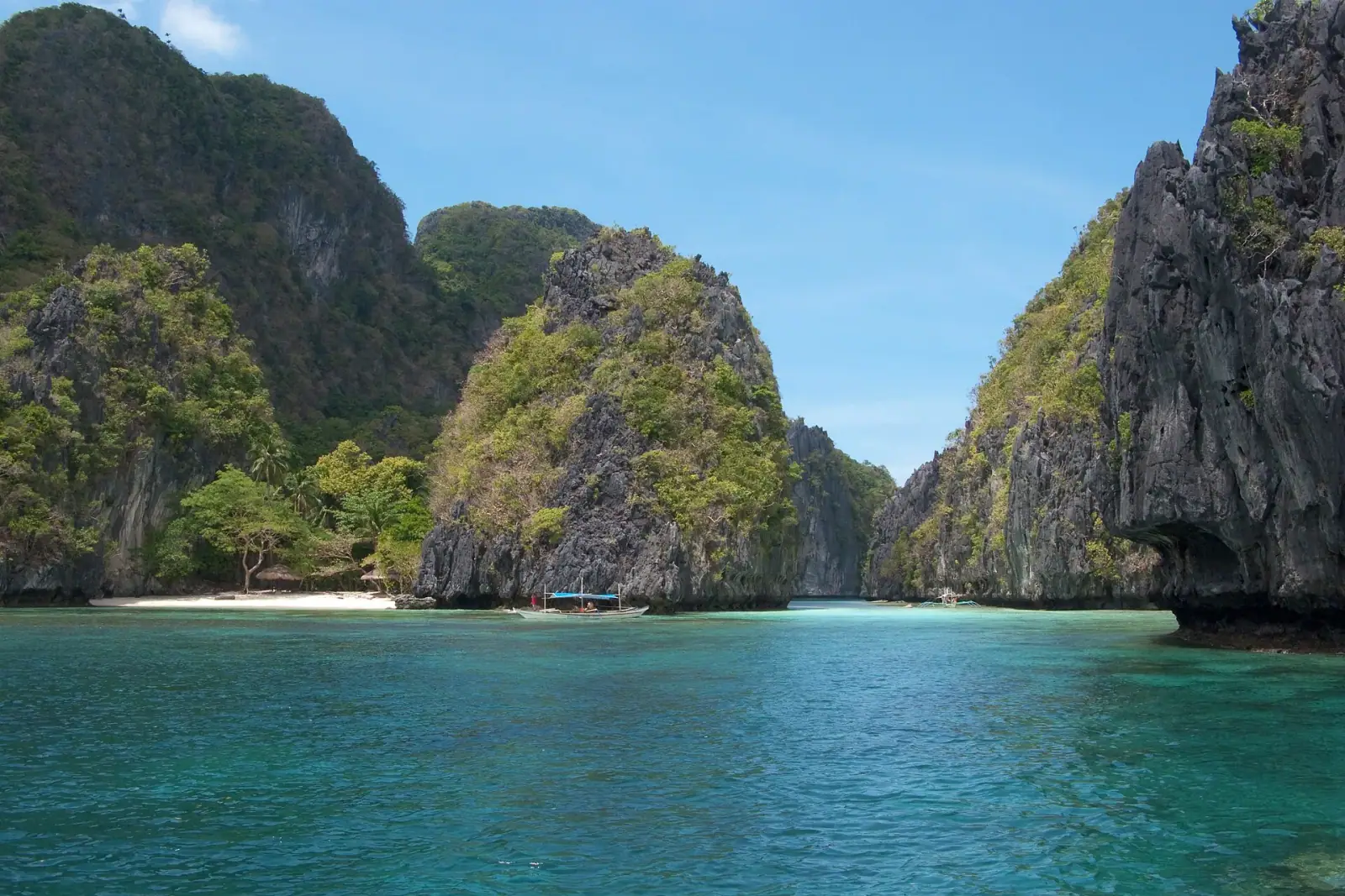 Turquoise lagoon surrounded by dramatic limestone karst mountains with white sand beach in Bacuit Bay, El Nido, Palawan, Philippines