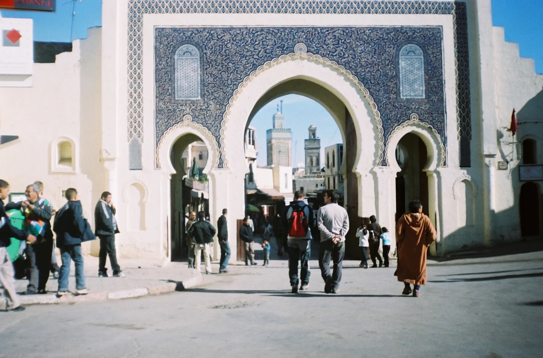 The Bab Bou Jeloud, the blue-tiled monumental gate to the medina of Fes, its three horseshoe arches framing the minarets of the old city, with people passing through