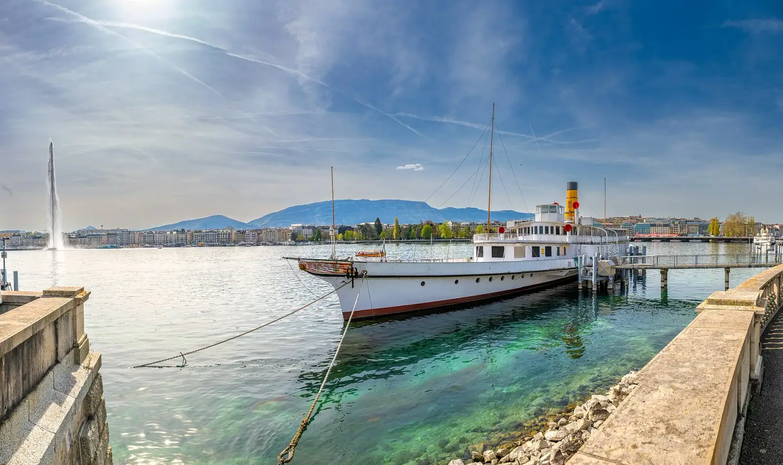 Lake Geneva with the Jet d'Eau fountain, city skyline, and mountains