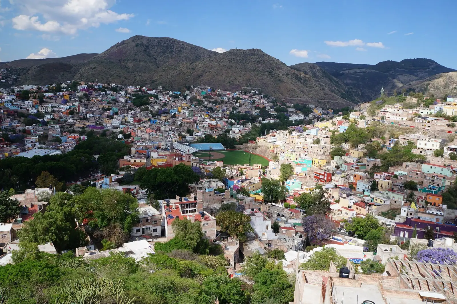 Panoramic view of Guanajuato, Mexico, showing colorful colonial buildings spread across a valley with mountains in the background