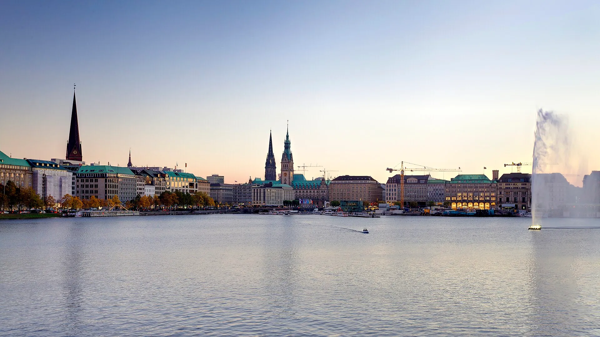 Hamburg skyline with Rathaus and church spires reflected across the Binnenalster lake at dusk