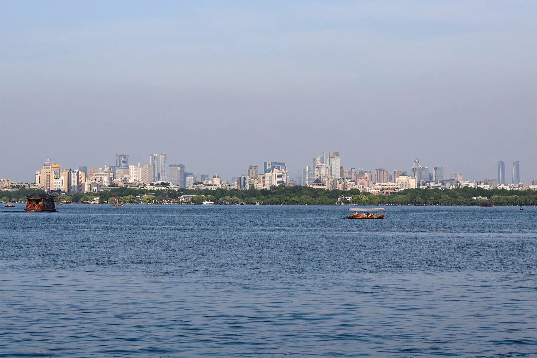 Hangzhou West Lake with a traditional boat and the city skyline across the water