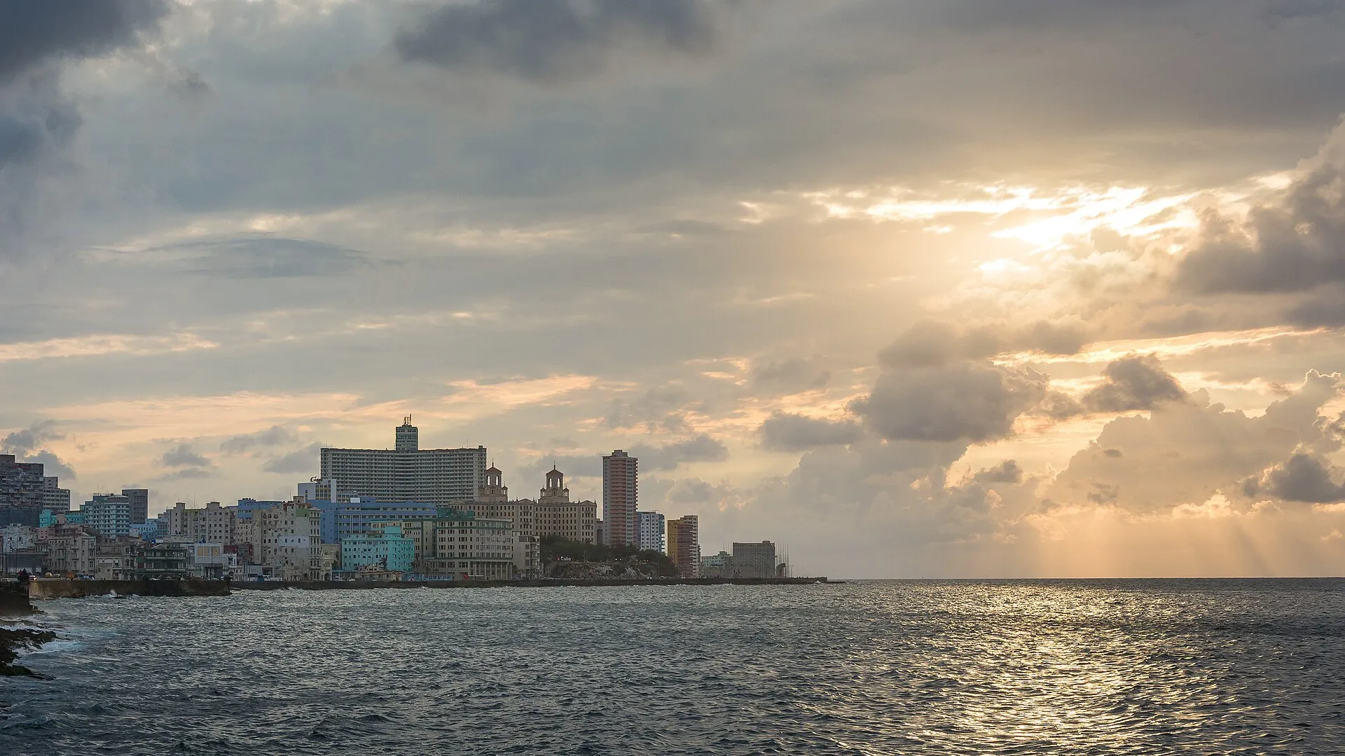 Golden evening light over the Havana seafront, with the Malecon and the Vedado skyline including the Hotel Nacional seen across the water