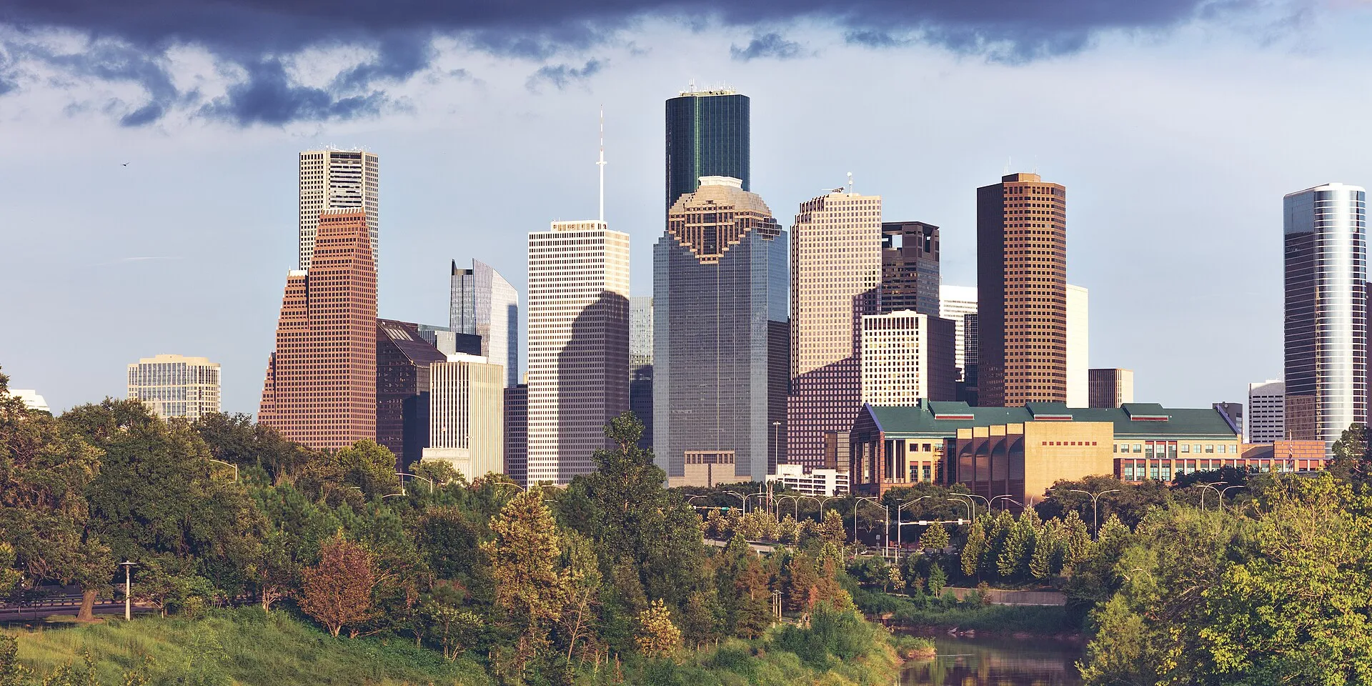 Downtown Houston skyscrapers glowing in golden evening light above the green treeline of Buffalo Bayou