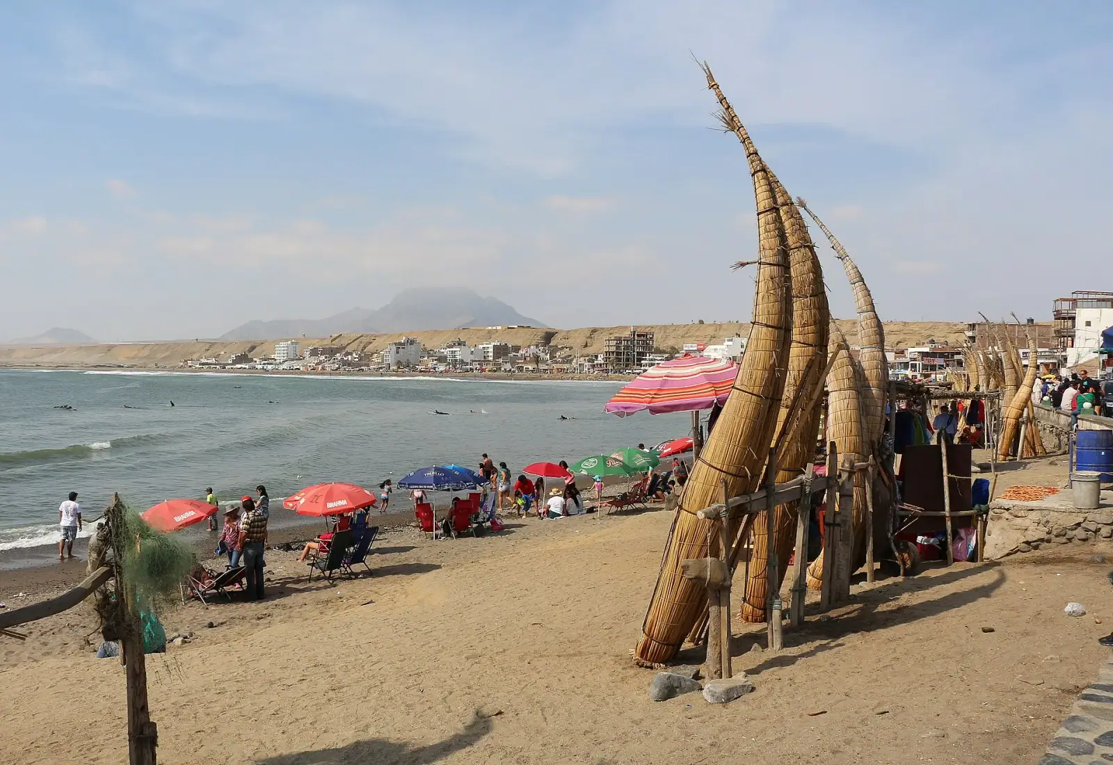 Huanchaco beach with traditional totora reed boats (caballitos de totora) in foreground and the coastal city and desert hills behind