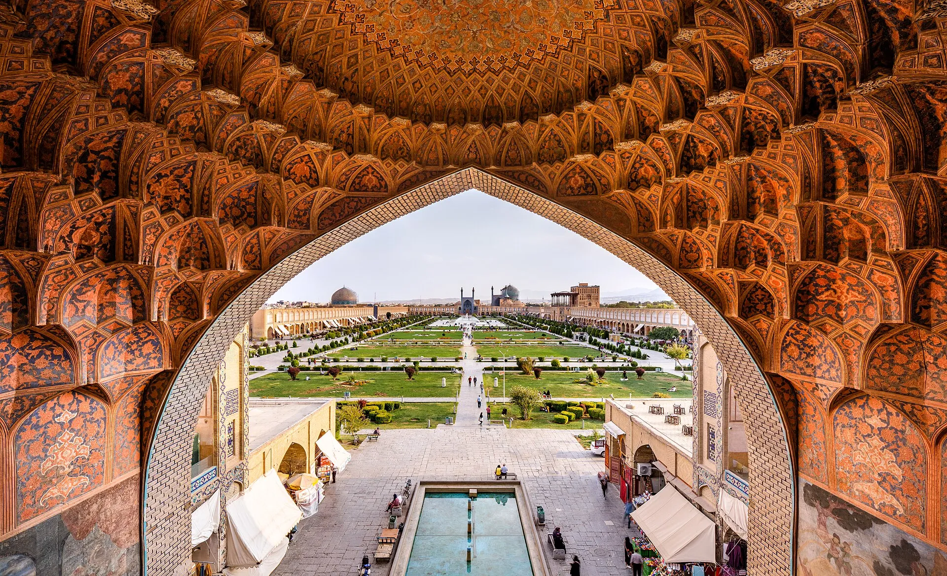 Naqsh-e Jahan Square in Isfahan framed by the honeycomb tiled vault of the Qeysarieh gate, with the Shah Mosque domes in the distance