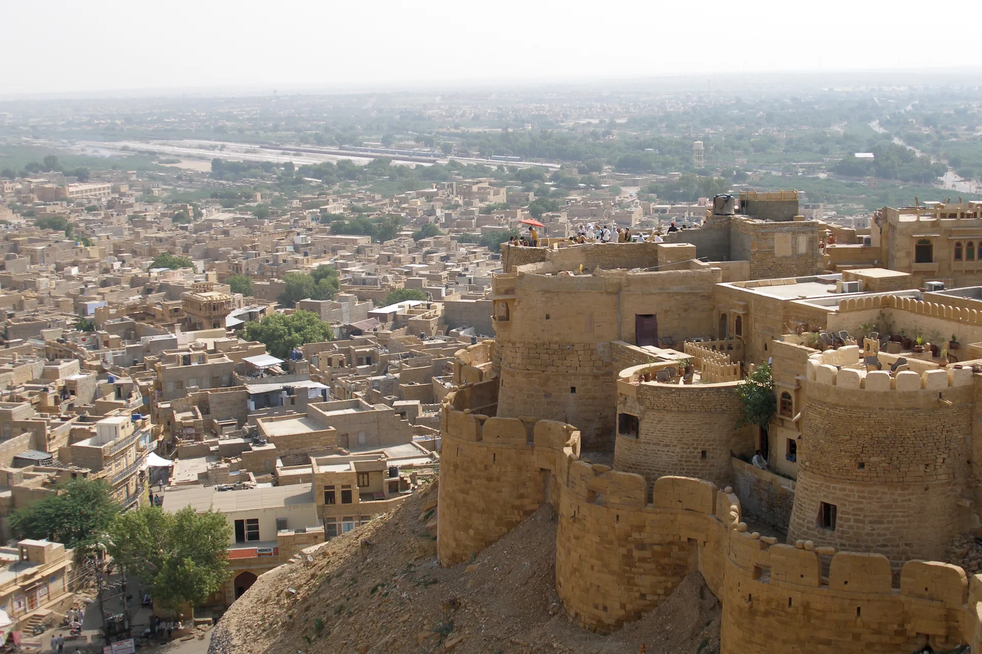 The golden sandstone bastions and ramparts of Jaisalmer Fort in the foreground, with the honey-coloured Golden City spreading across the Thar Desert plain below
