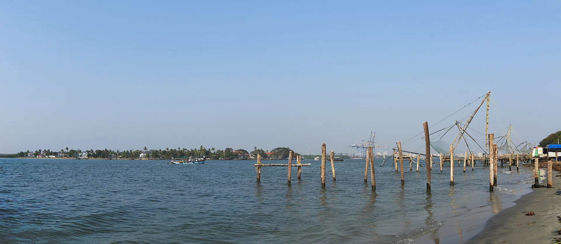 Chinese fishing nets at Fort Kochi waterfront with coconut palms and blue sky