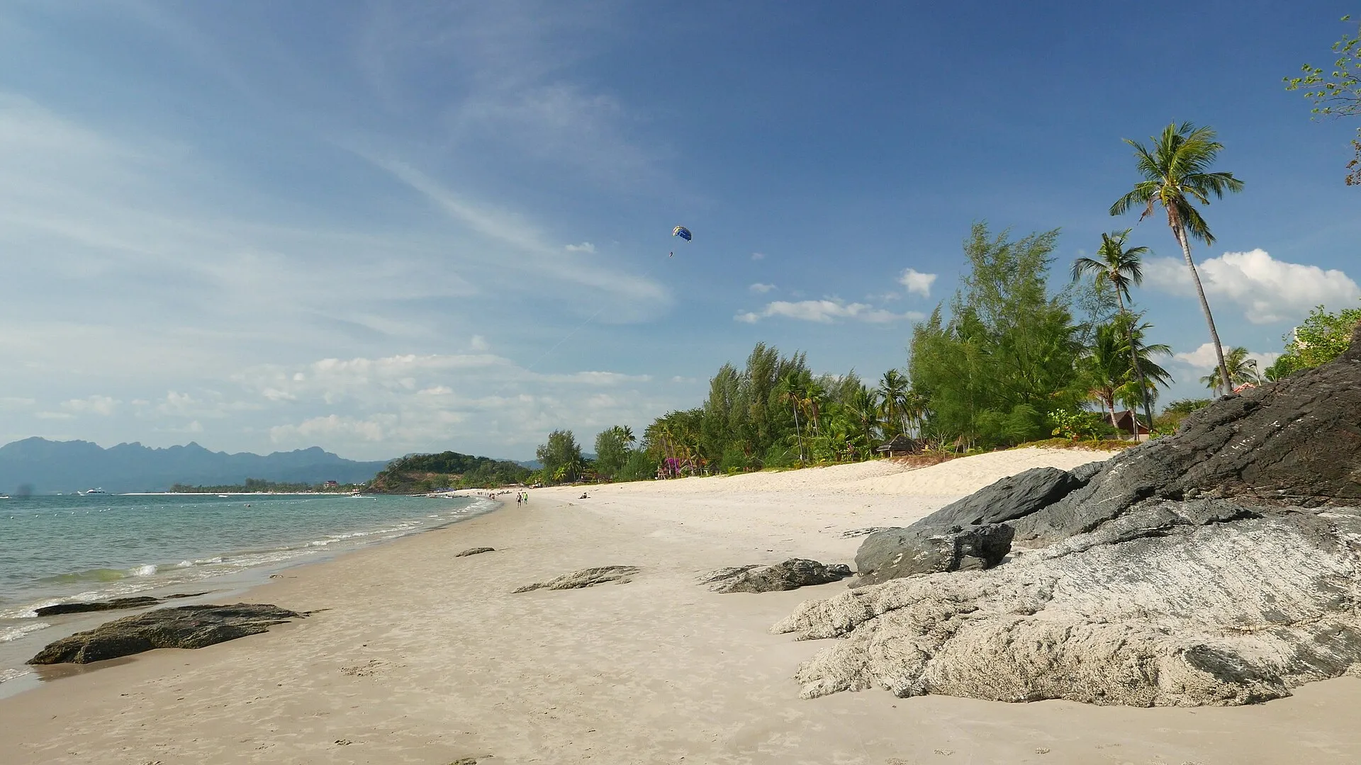 Pantai Cenang beach with white sand, turquoise water, palm trees and mountains in Langkawi, Malaysia