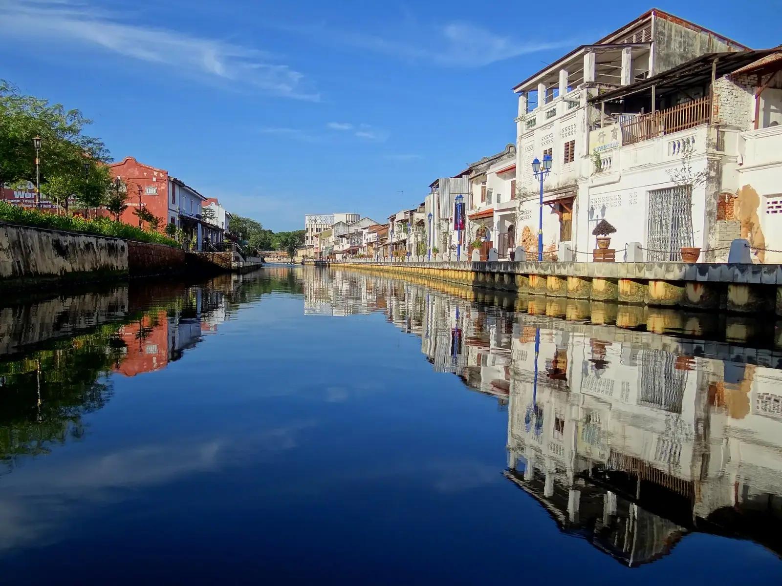 Historic shophouses reflected in the calm Malacca River on a clear blue-sky morning