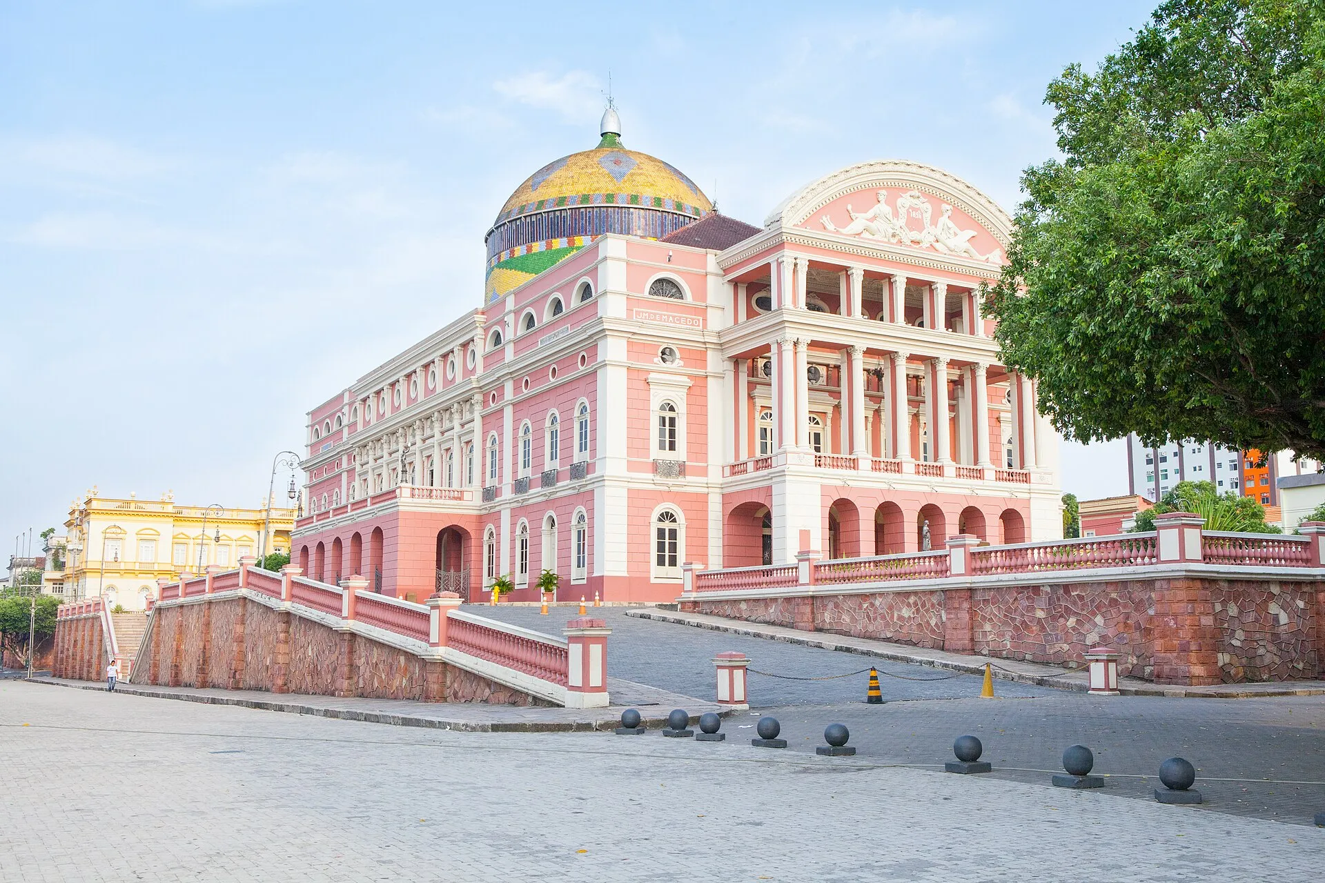 The pink and cream facade and coloured tiled dome of the Teatro Amazonas opera house in Manaus under a clear blue sky