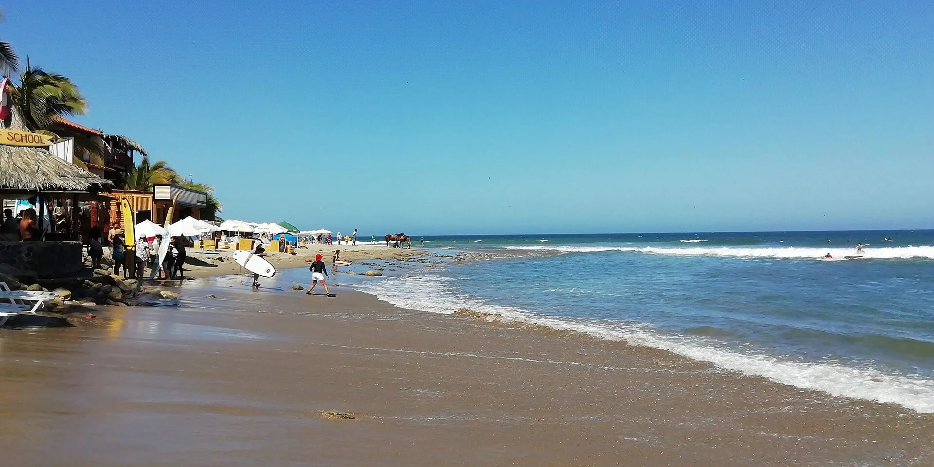 Máncora beach with surf school, surfers and beachgoers on a bright sunny day