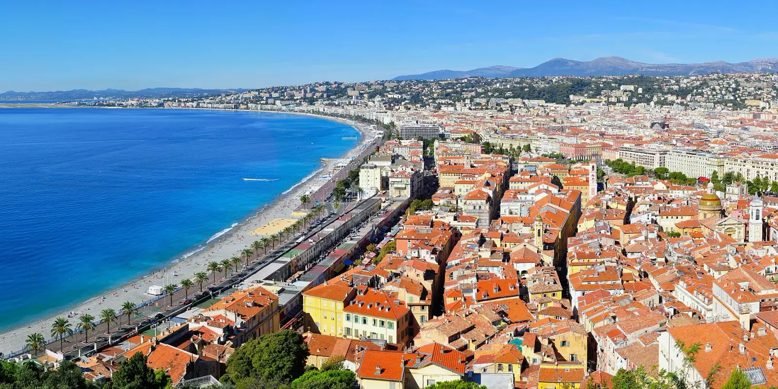 Panoramic view of Nice, France, showing the Bay of Angels, Promenade des Anglais beach, and terracotta rooftops of the Old Town