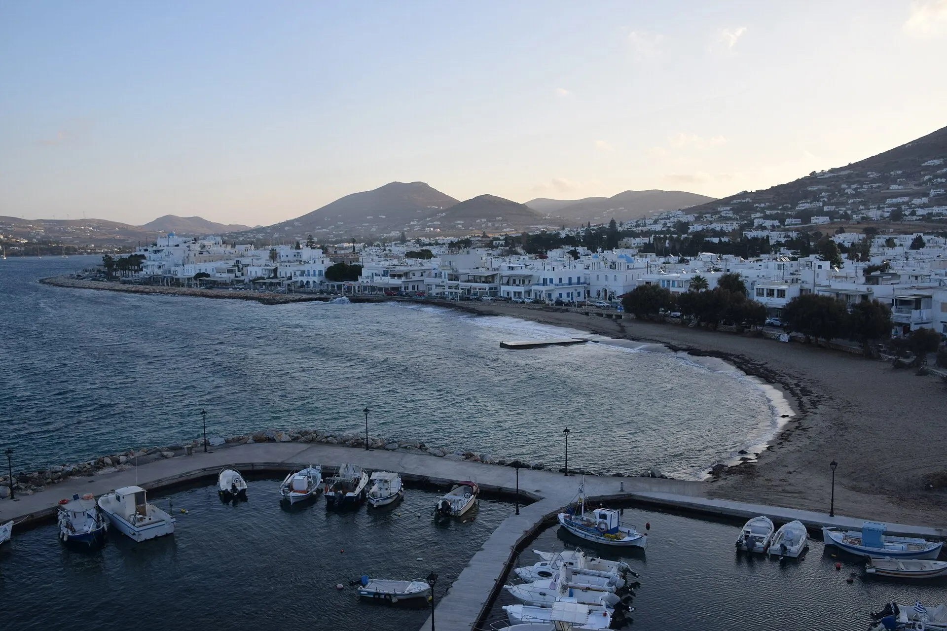 The bay and white houses of Paros at dusk, with fishing boats moored below