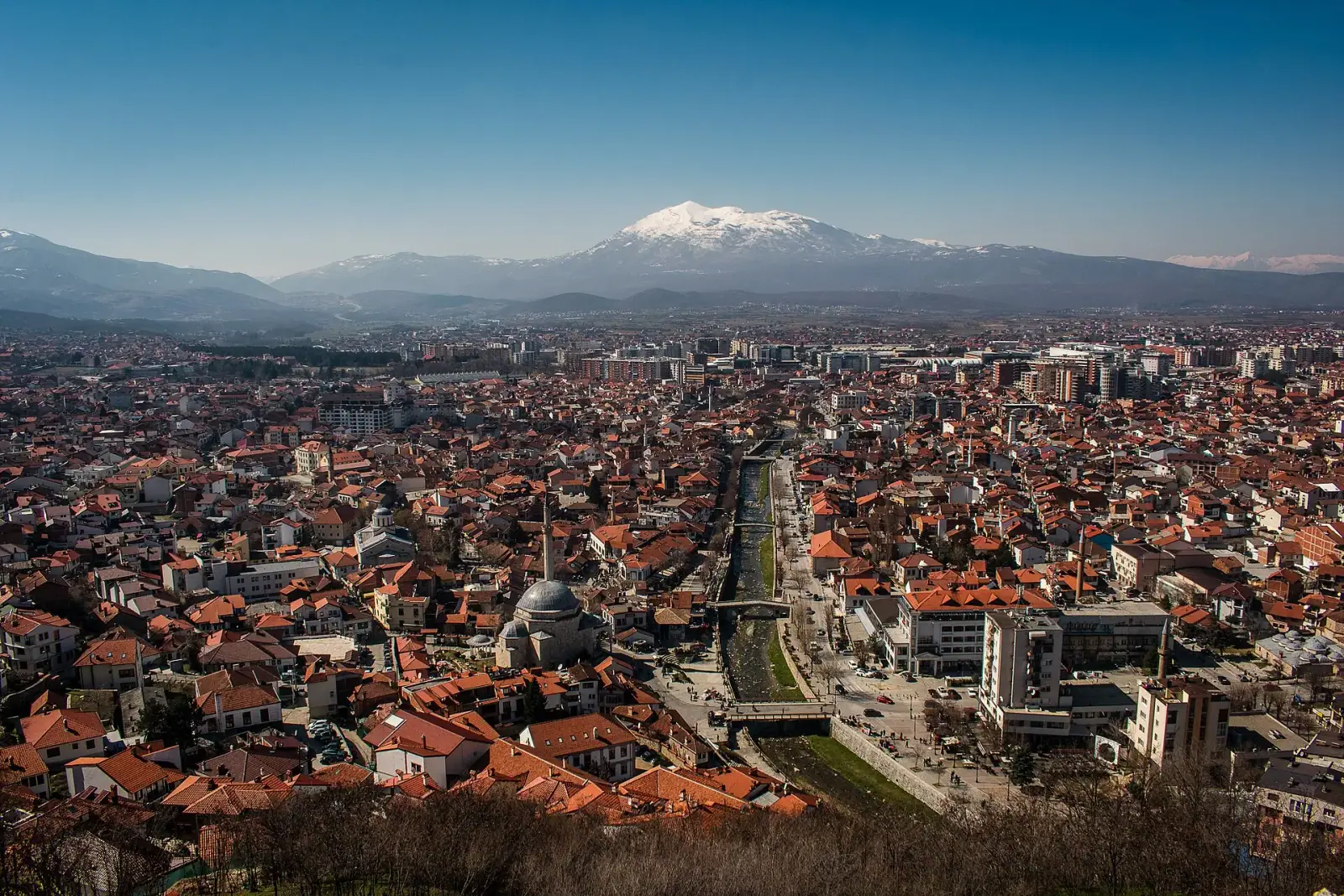 Prizren cityscape with the Sinan Pasha Mosque, the Bistrica river, and the snow-capped Sharr mountains in the background