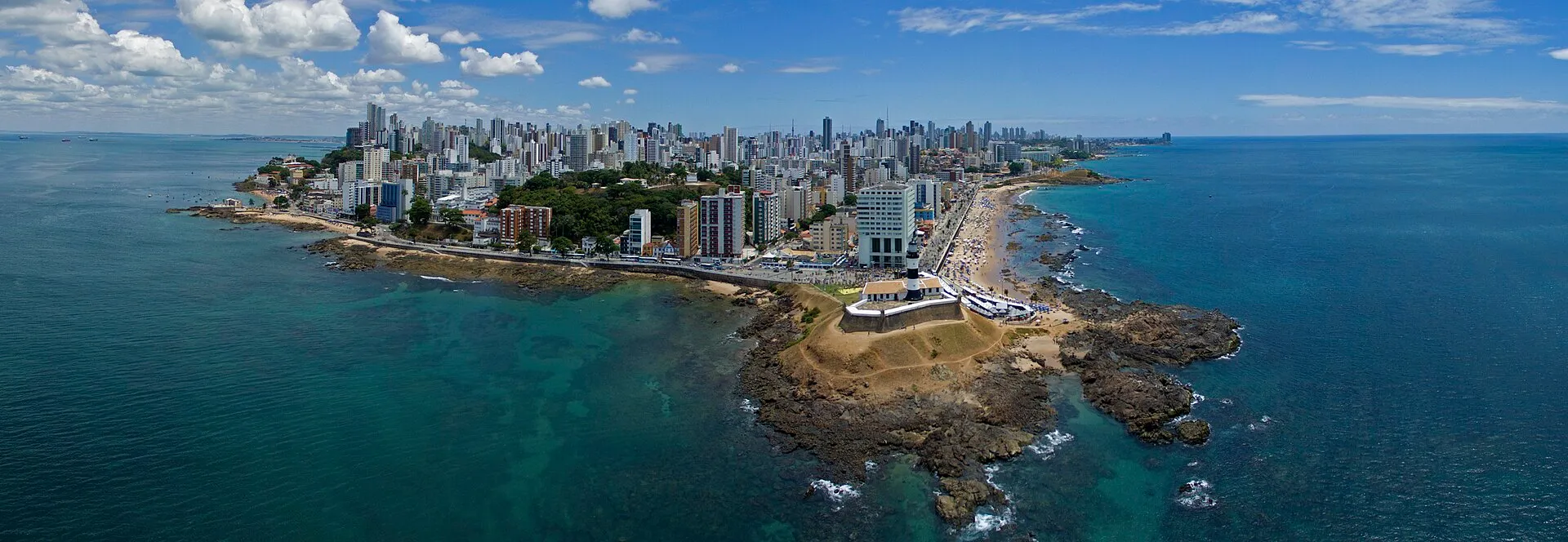 Aerial panorama of Salvador, Bahia, showing Farol da Barra lighthouse and fort on the peninsula with the city skyline behind
