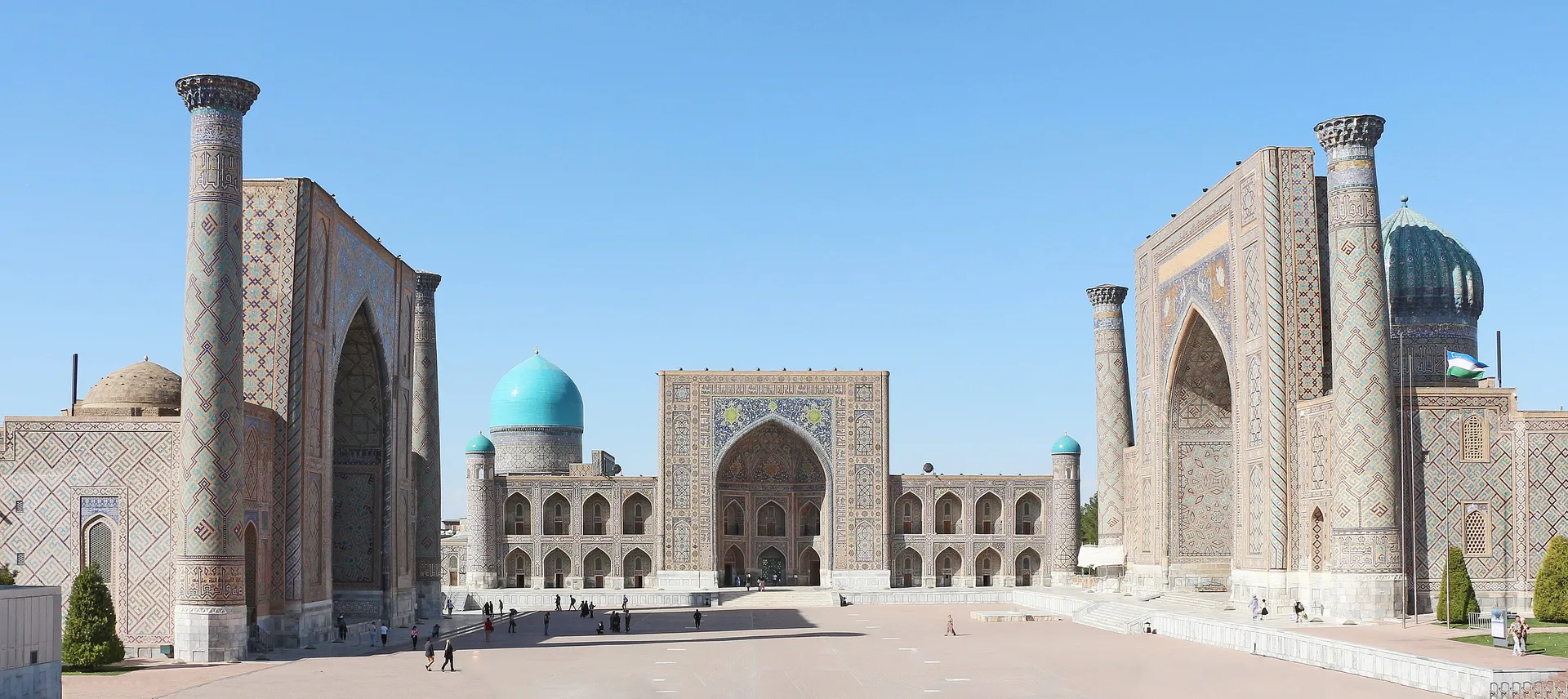 The Registan in Samarkand, three Islamic madrasahs with towering portals, ribbed turquoise domes and tiled minarets around a public square under a clear sky