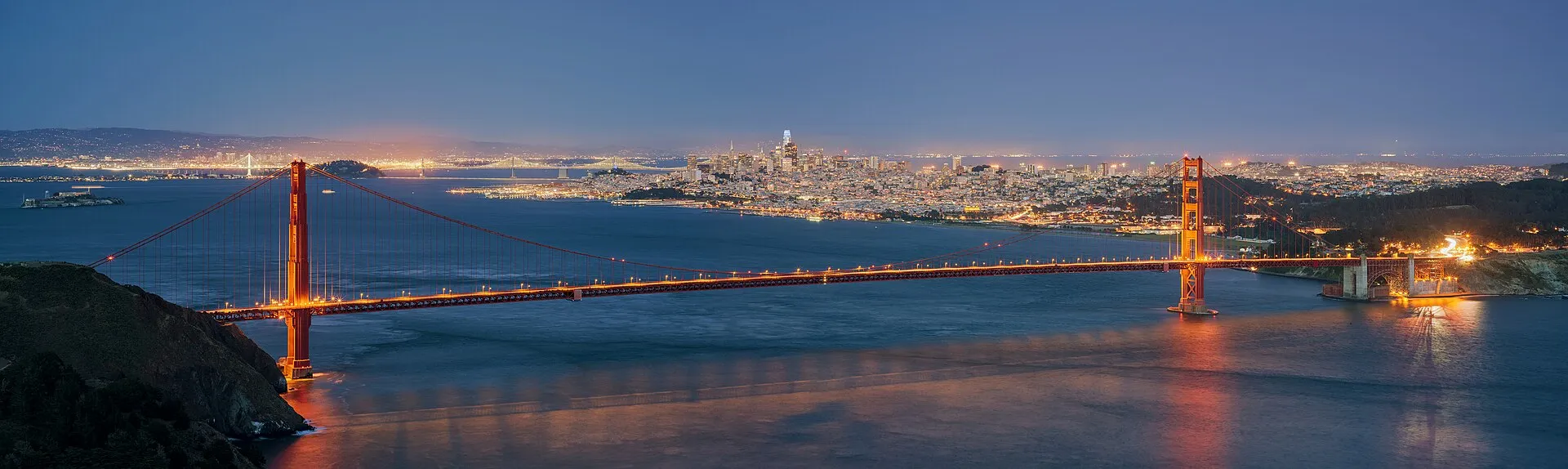 The Golden Gate Bridge with the San Francisco downtown skyline behind it, viewed from Hawk Hill at blue hour