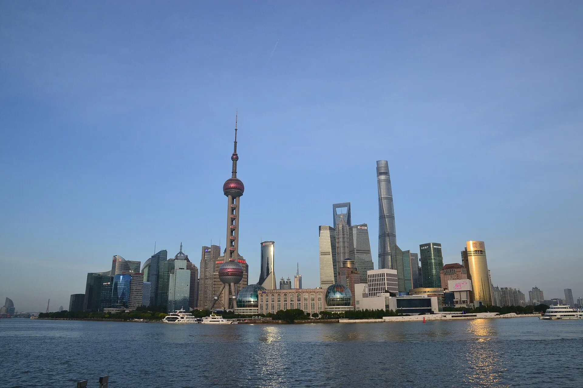 The Pudong skyline seen across the Huangpu River in late afternoon light, with the Oriental Pearl Tower and Shanghai Tower standing above the waterfront