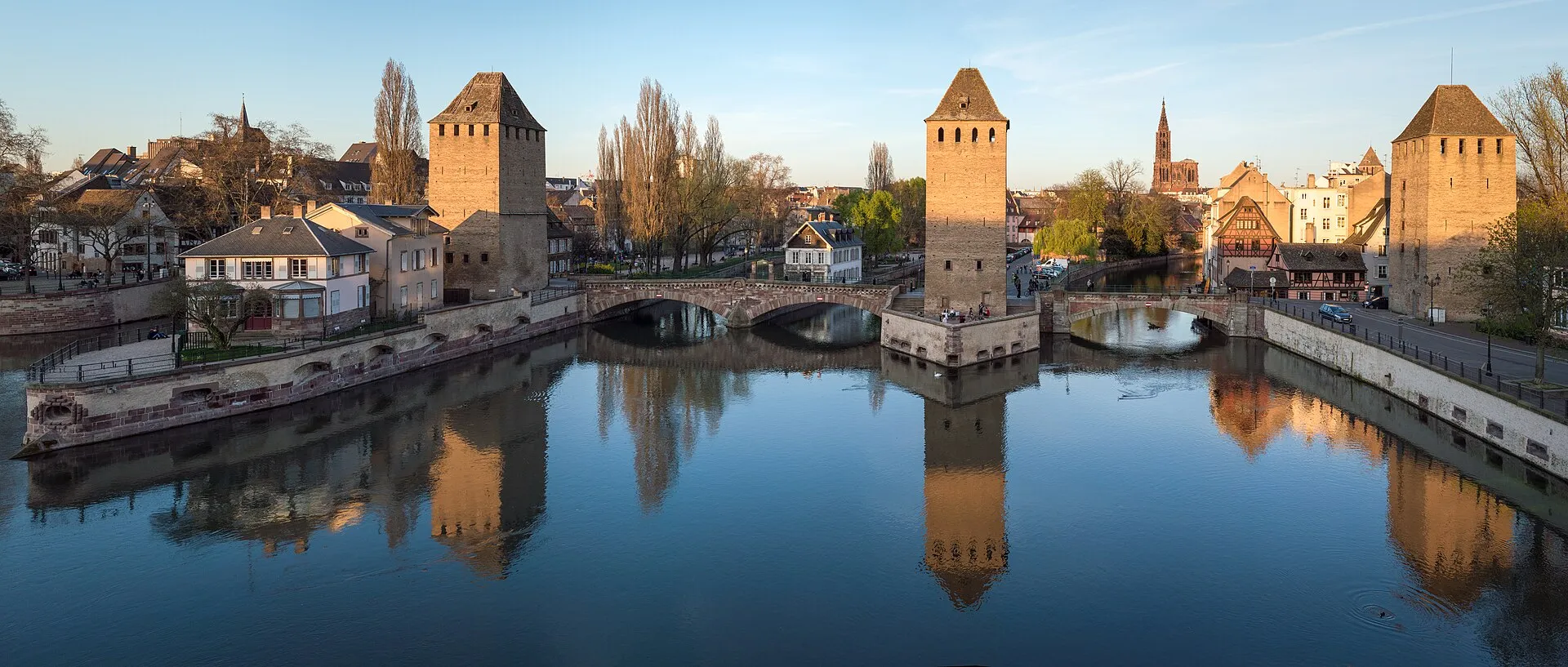Strasbourg Ponts Couverts covered bridges reflected in the Ill River at golden hour, cathedral spire in the background