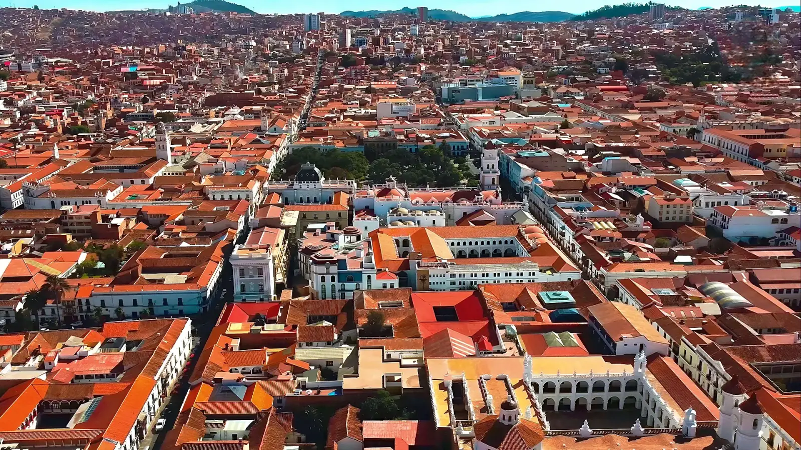 Aerial view of Sucre, Bolivia, showing the historic white colonial city centre with red-orange tile rooftops and Plaza 25 de Mayo