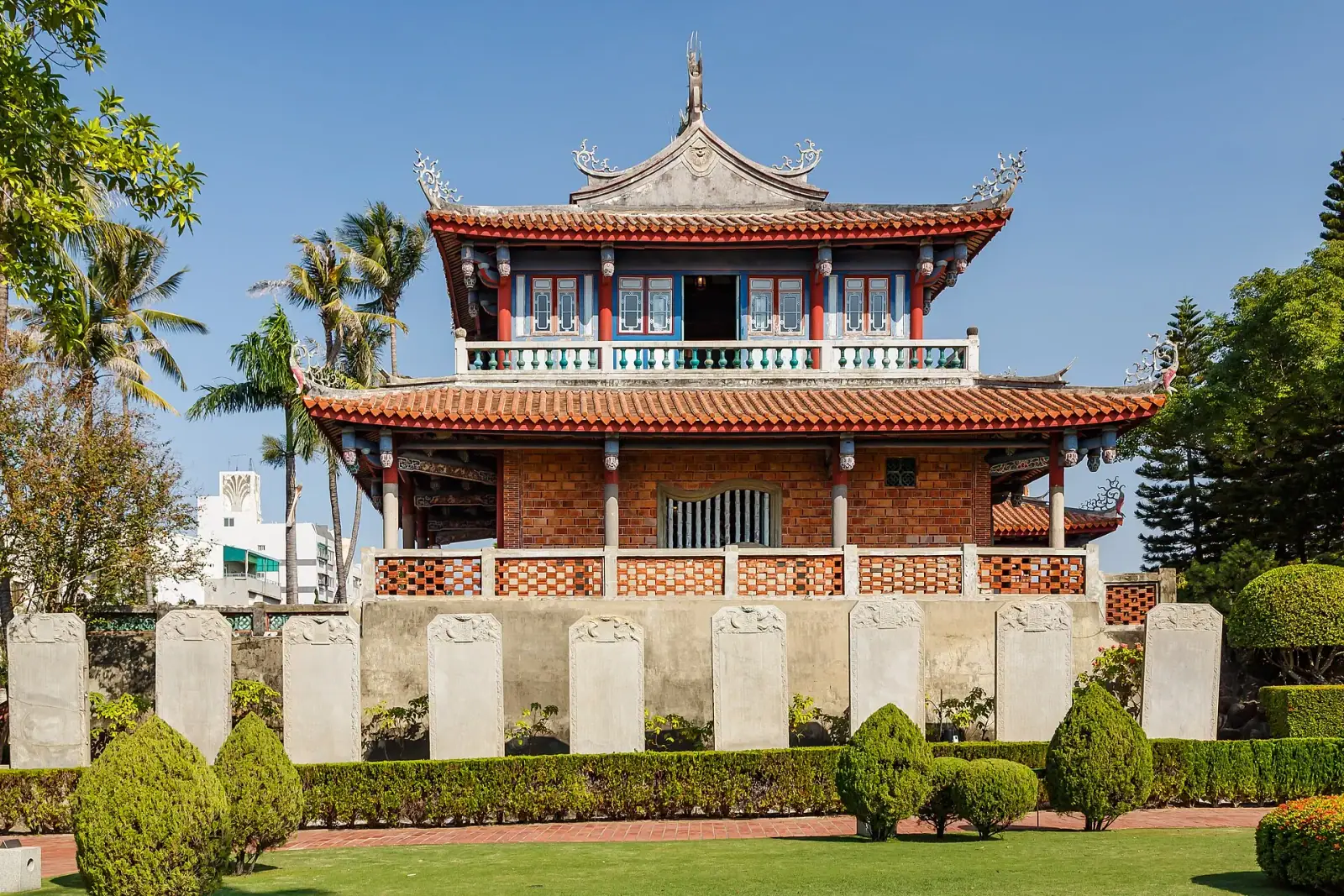 Chihkan Tower (Fort Provintia) in Tainan, a two-tier red-brick pavilion behind a row of stone stele and a manicured garden under a clear blue sky