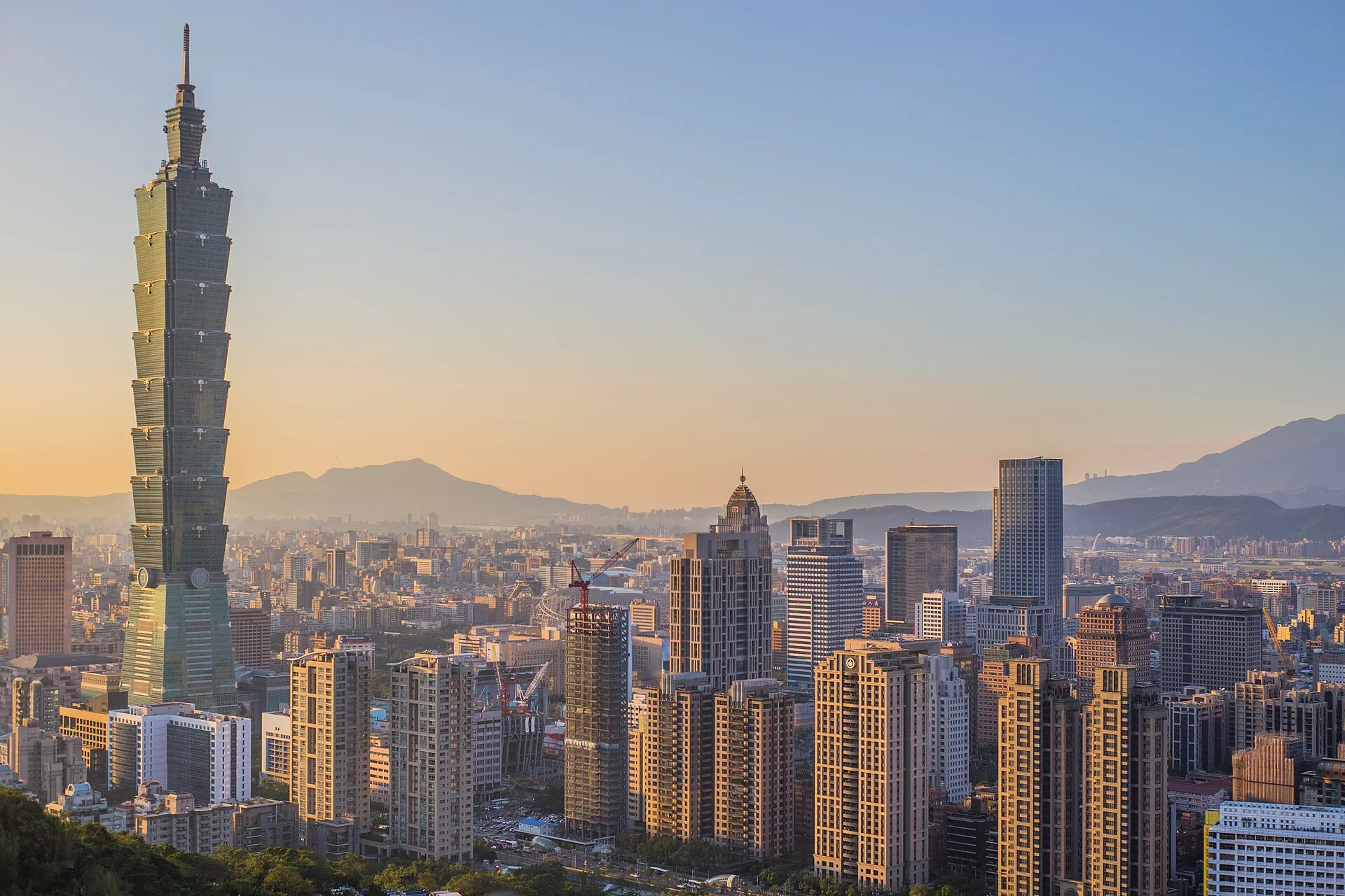 Taipei 101 tower dominating the city skyline at golden hour with mountains in the background