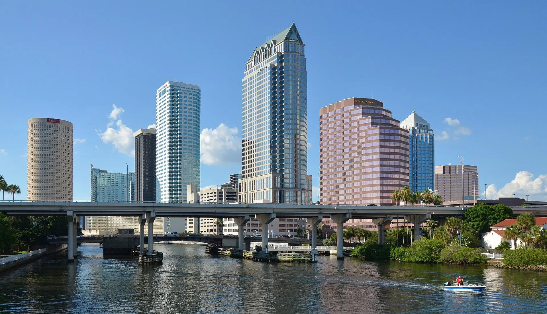 Downtown Tampa towers rising above the Hillsborough River under a clear blue sky with a small boat passing by