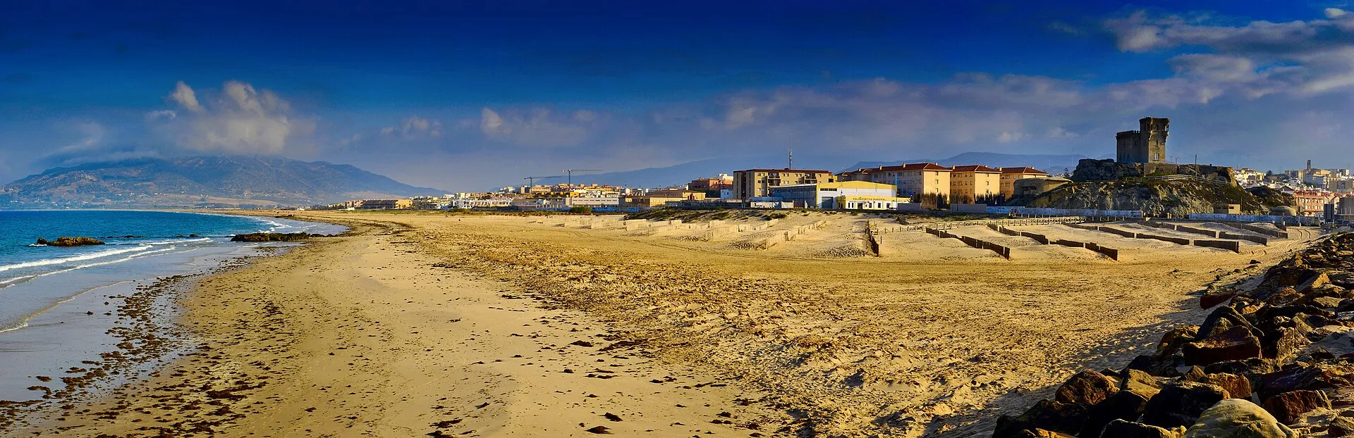 Panoramic view of Tarifa beach, old town, and castle tower with mountains behind