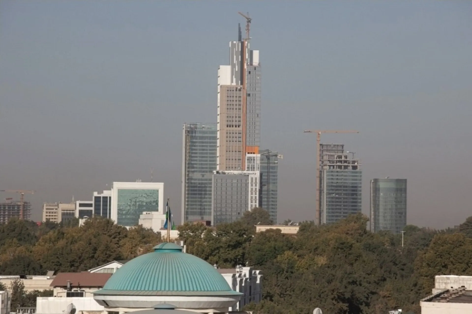 Modern high-rise towers of the Tashkent City skyline rising above green parkland and a turquoise dome