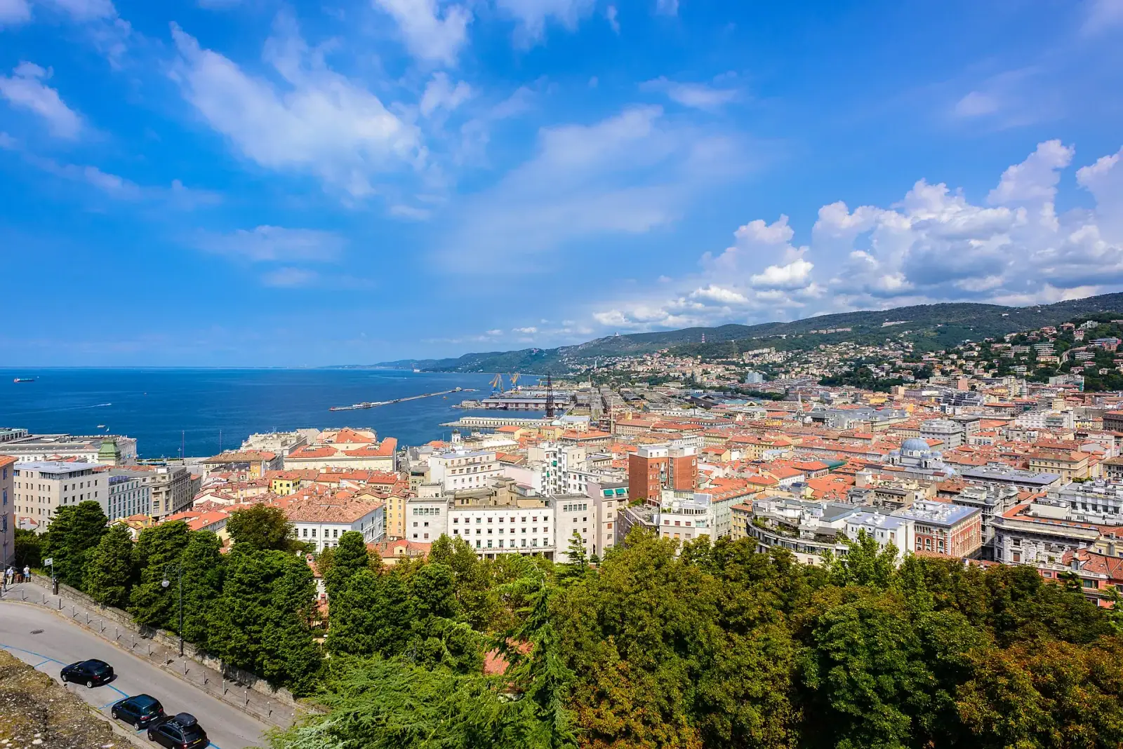 Aerial view of Trieste cityscape with orange rooftops, the Adriatic Sea, and green hills