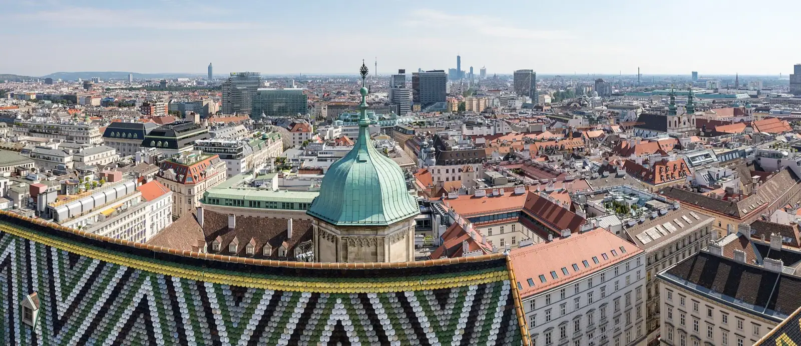 Vienna cityscape panorama viewed from the south tower of Stephansdom, showing the iconic tiled roof and city stretching to the horizon