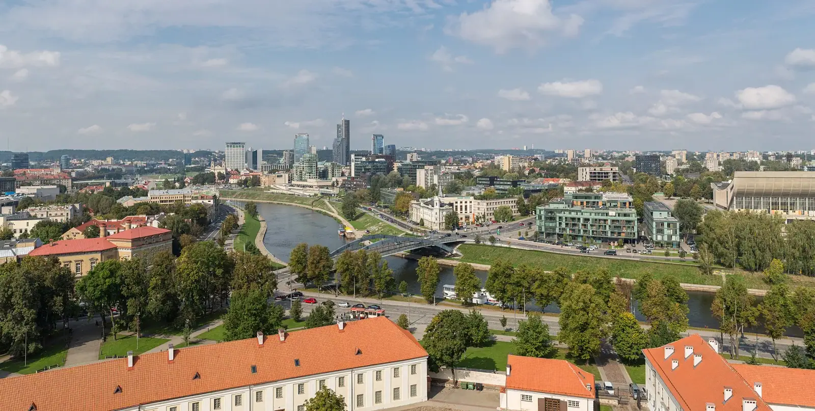 Panoramic view of Vilnius showing the Neris River, old town with orange-tiled rooftops, and modern Snipiskes business district skyline