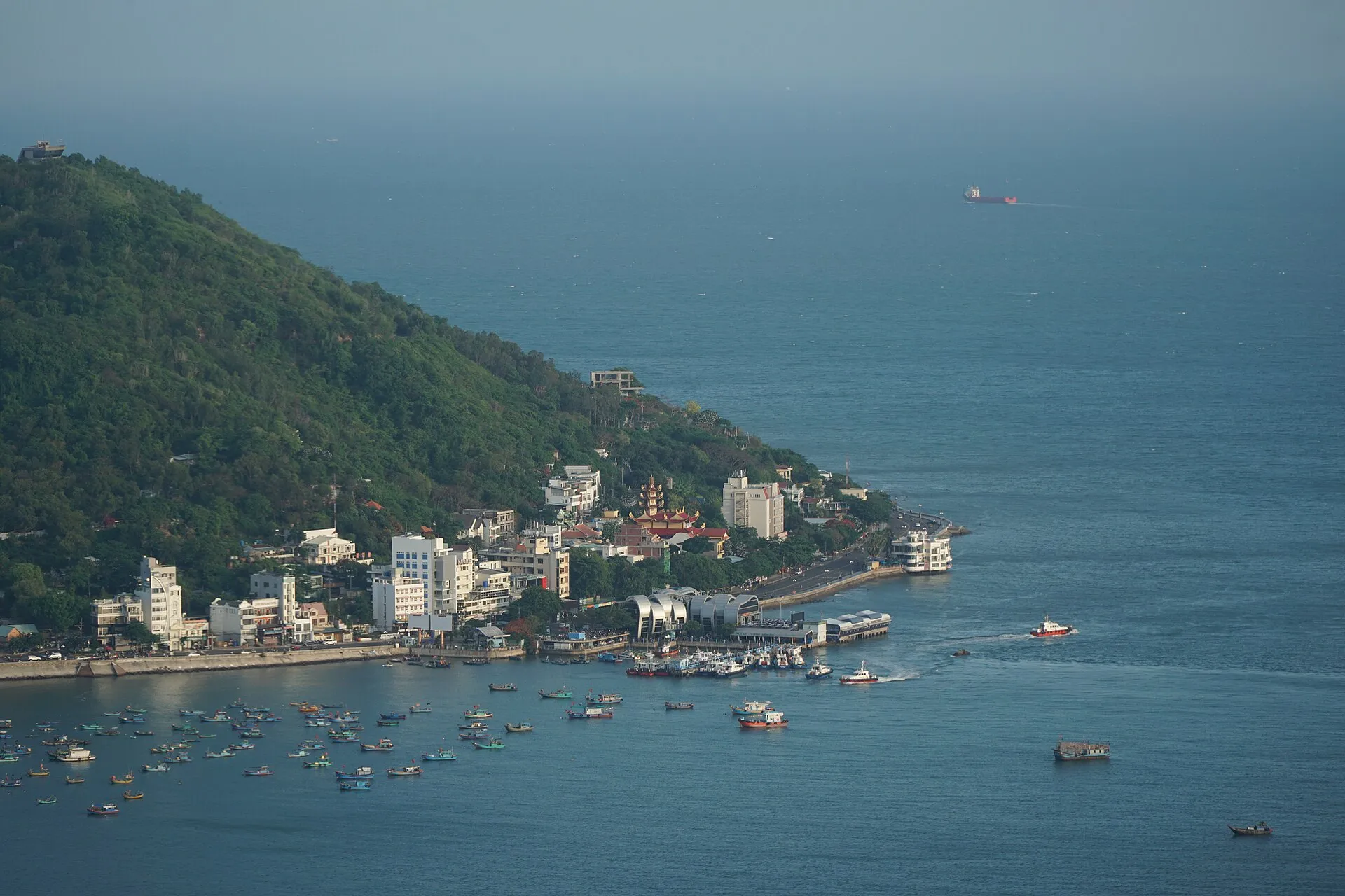 Elevated view over Front Beach in Vung Tau, Vietnam, with colourful fishing boats moored in the bay below the green slopes of Small Mountain.