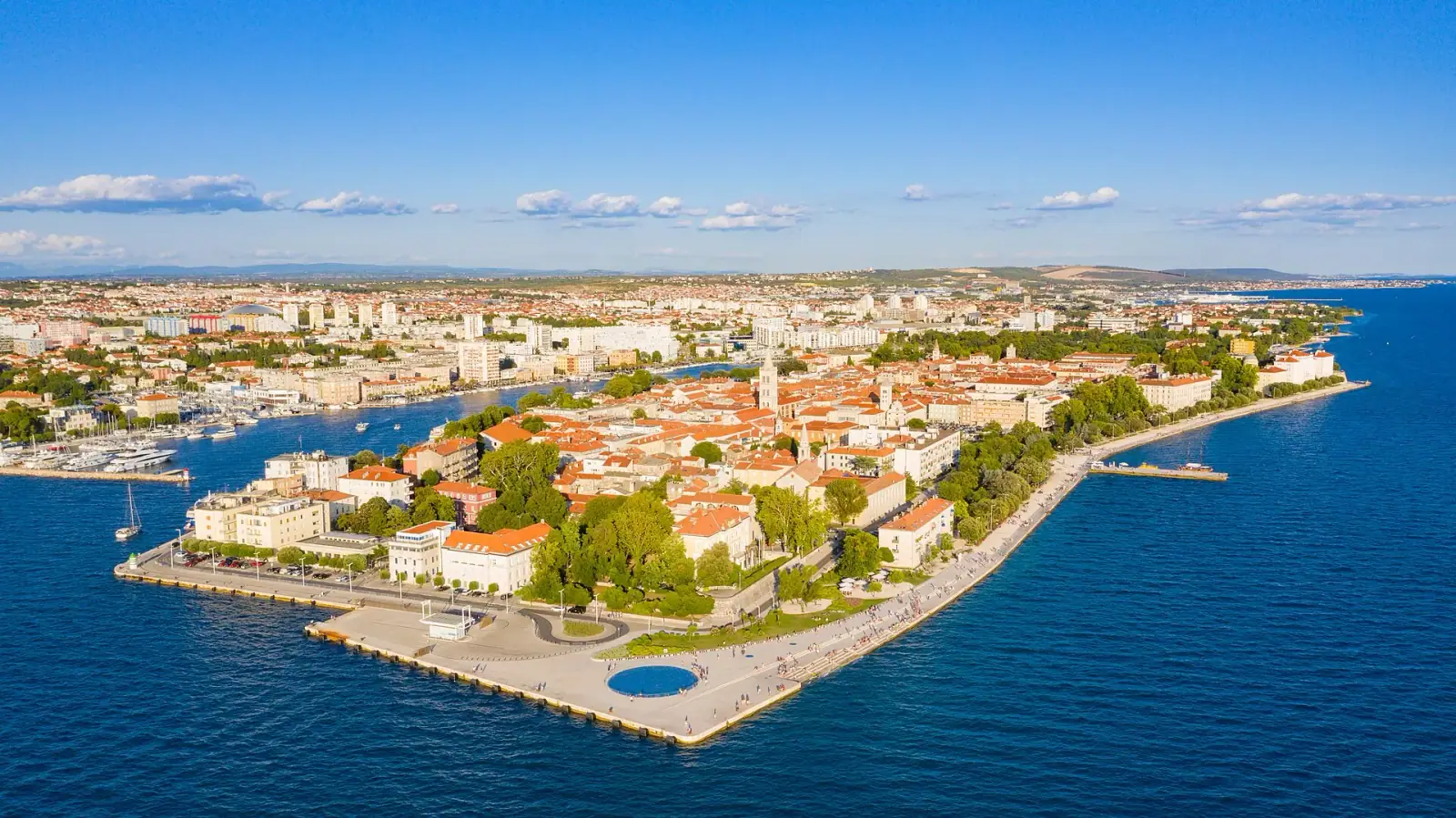 Aerial view of Zadar old town peninsula surrounded by the Adriatic Sea, with the Greeting to the Sun circular installation on the waterfront promenade