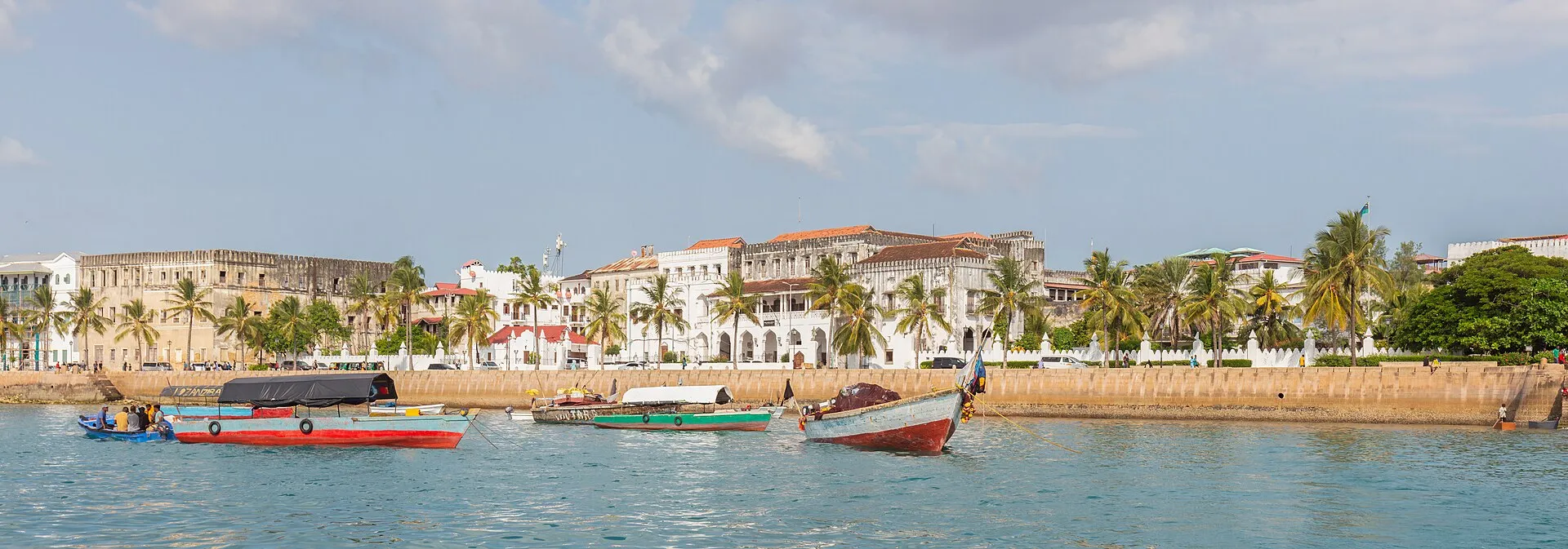 Stone Town waterfront with colourful wooden boats on turquoise water and the Sultan's Palace in the background